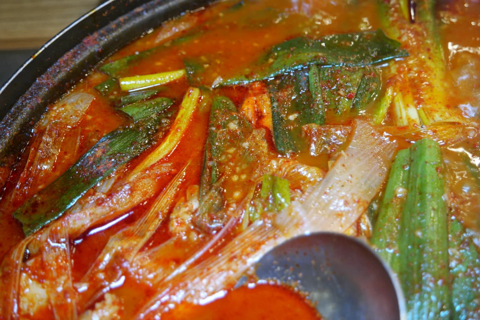 Scallion pieces floating on the surface of dakbokkeumtang broth before it reaches a full boil