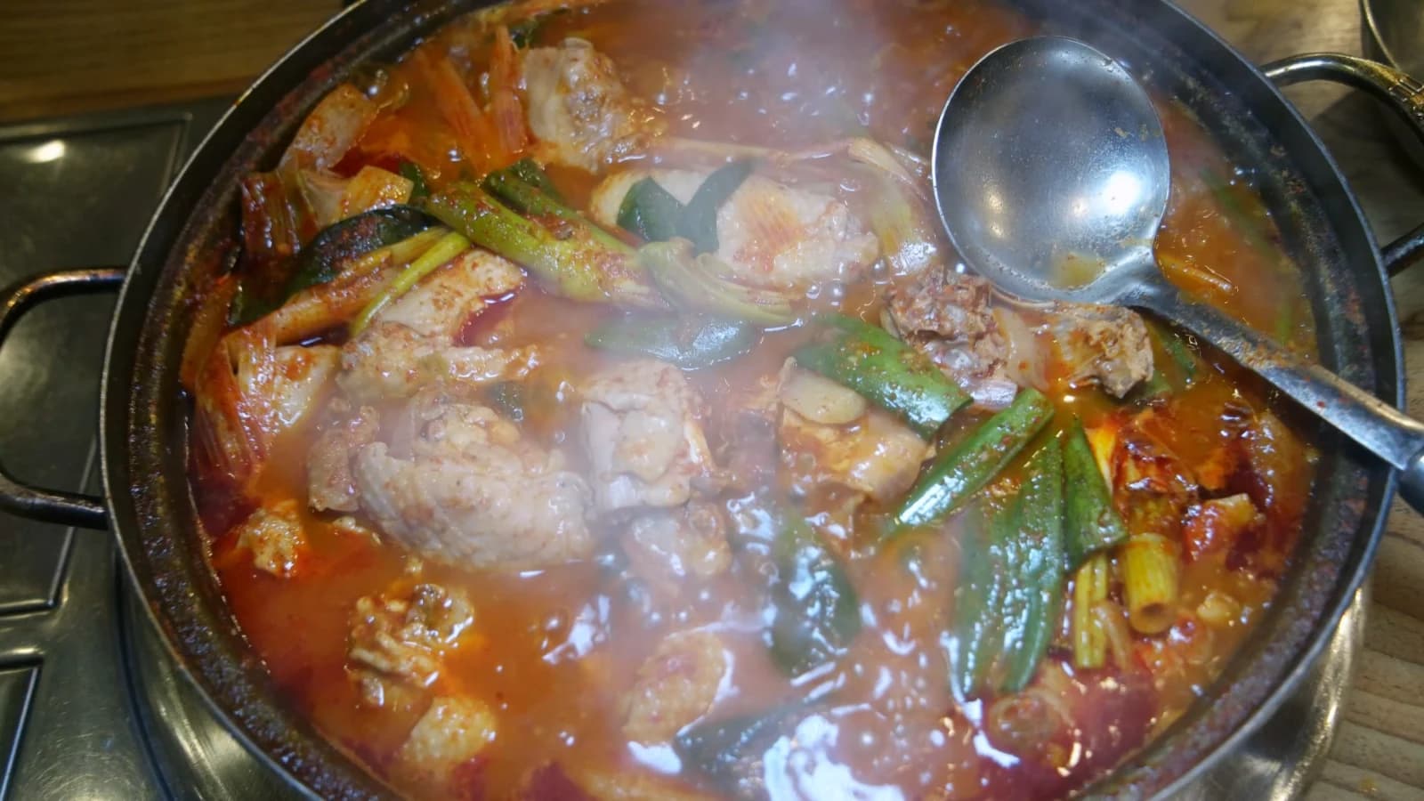 Steam rising from the dakbokkeumtang pot with drumstick and potato pieces visible through the broth