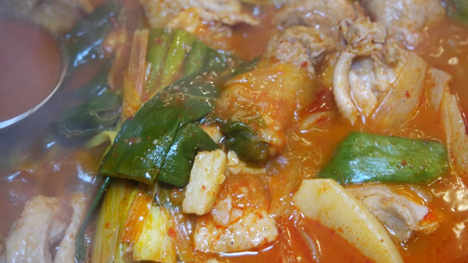 Close-up of chicken coated in red dakbokkeumtang sauce with scallions and carrots mixed in