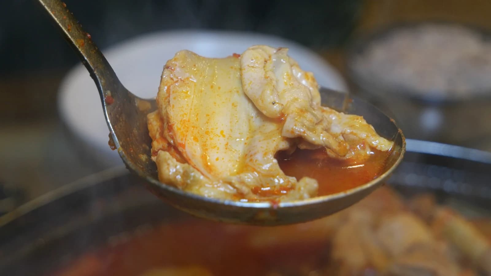 Close-up of ladled chicken piece showing red-coated exterior and pale cooked meat where it's pulling from the bone