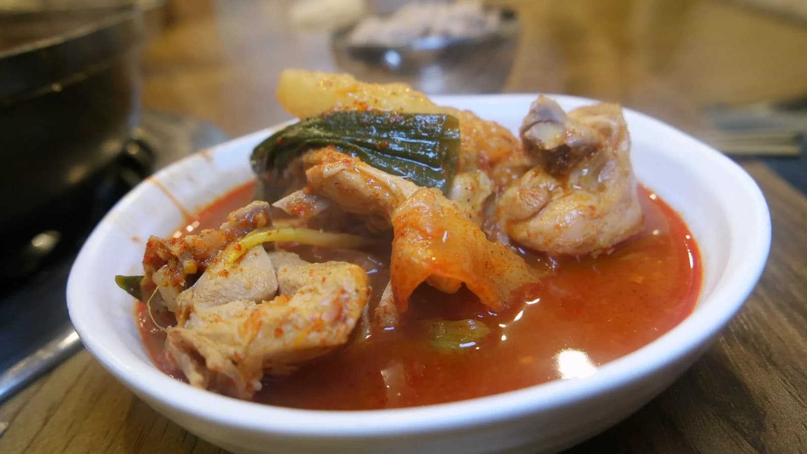 Individual plate with dakbokkeumtang chicken pieces, potato, and scallion in a shallow pool of red broth