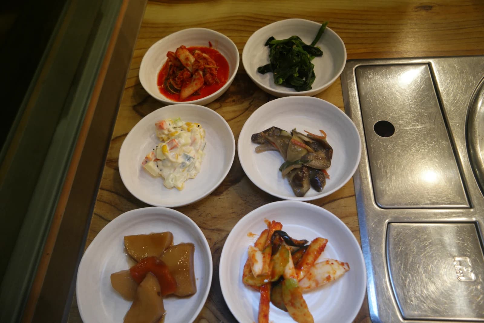 Six banchan side dishes served with dakbokkeumtang including kimchi, spinach, potato salad, eggplant, pickled radish, and stuffed cucumber