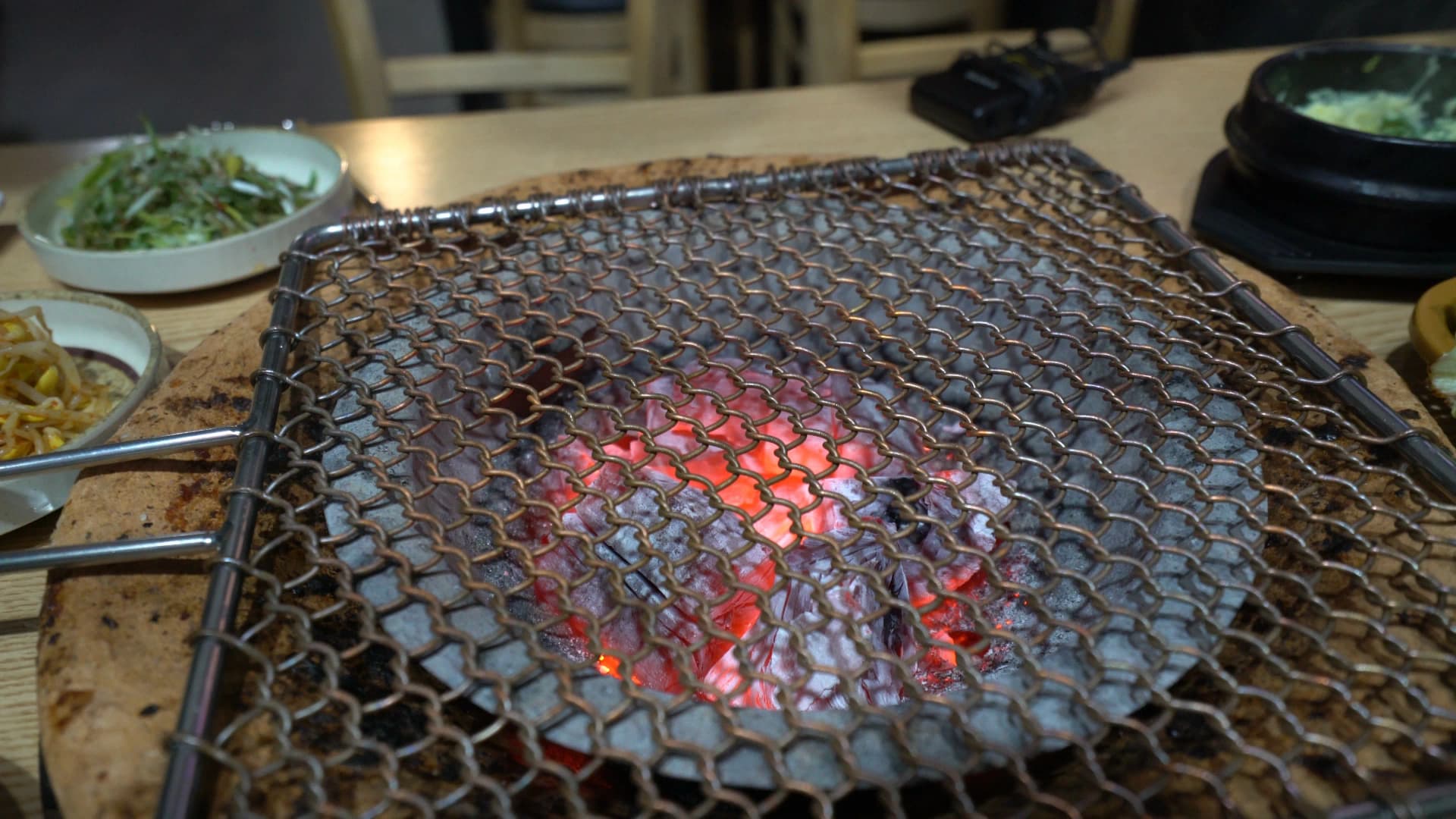 Glowing red charcoal beneath a perforated metal mesh grate set up for charcoal grilled chicken at a Korean BBQ table