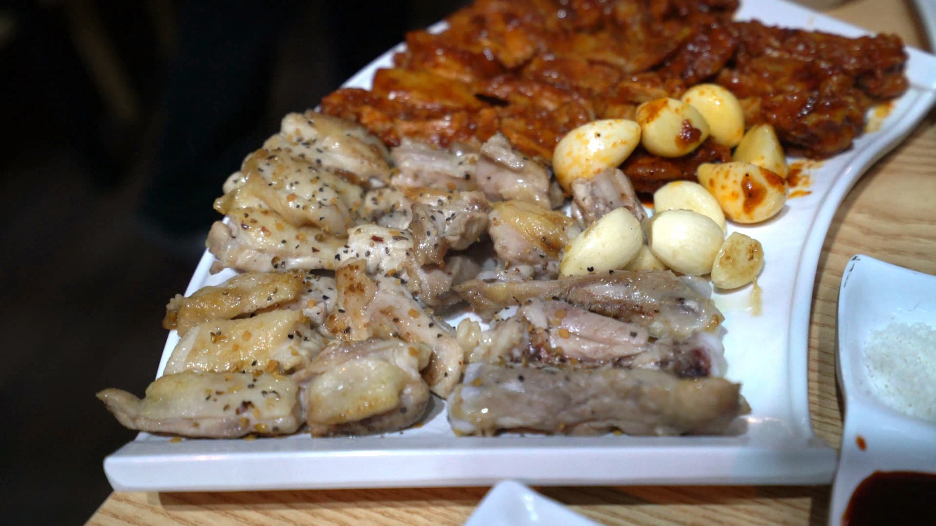 Plate of Korean BBQ chicken divided into salt-seasoned and gochujang spicy marinated portions with whole garlic cloves