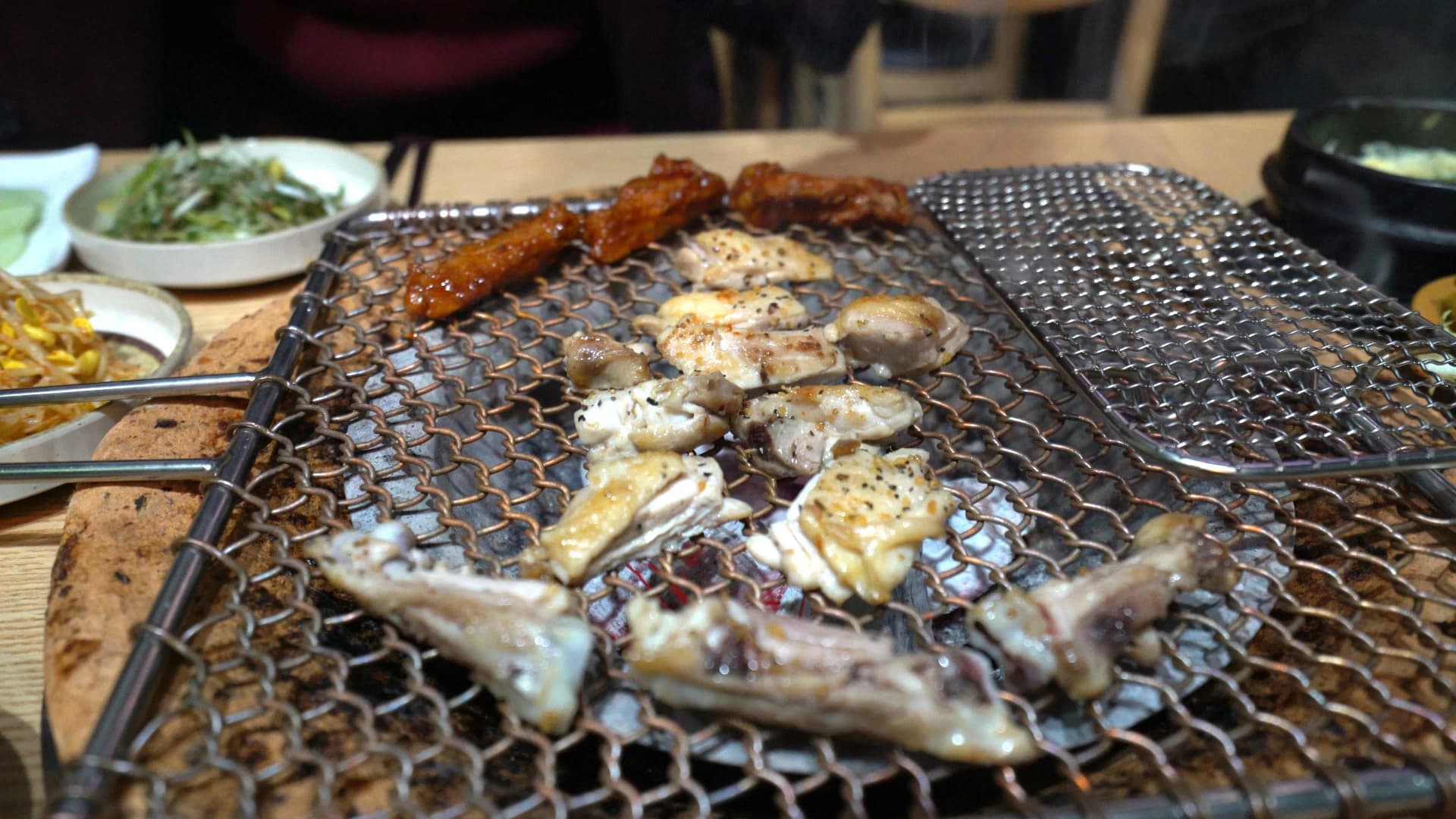 Salt-seasoned and gochujang marinated chicken pieces placed on a charcoal grill mesh grate starting to cook