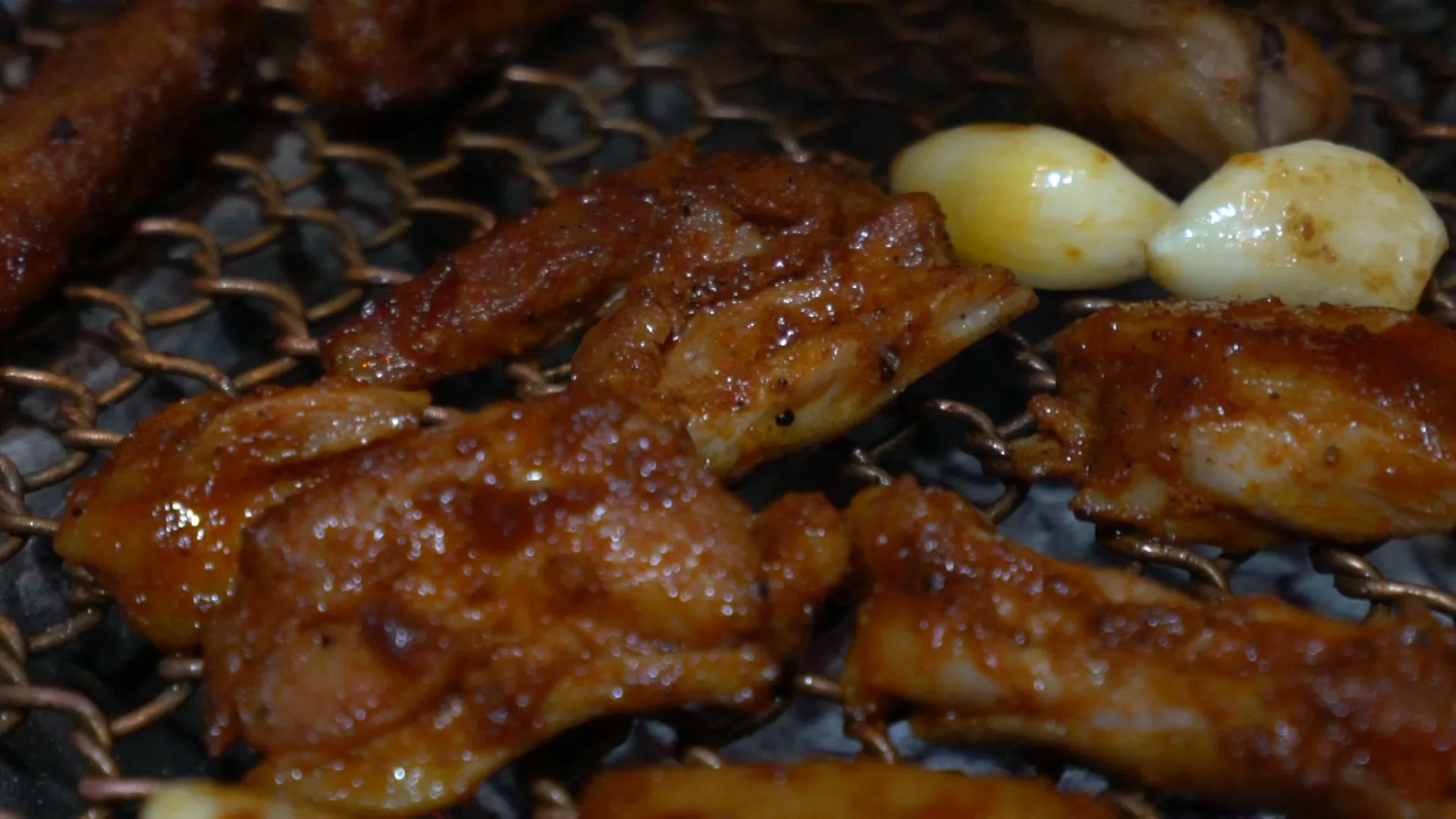 Close-up of gochujang spicy marinated dakgalbi bubbling and sizzling on a charcoal mesh grate