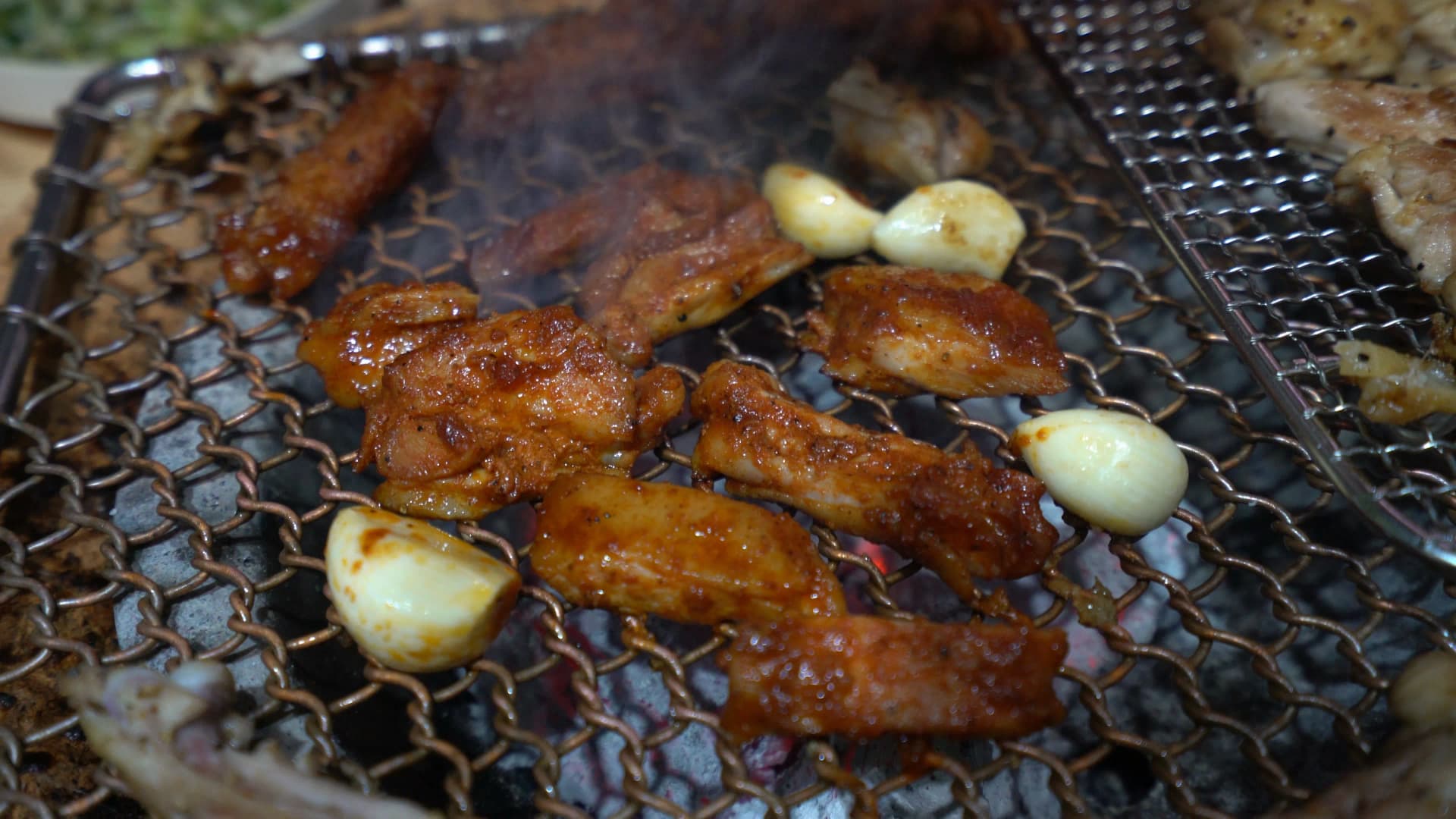 Wide shot of smoky charcoal grill with both gochujang marinated and salt-seasoned chicken cooking simultaneously