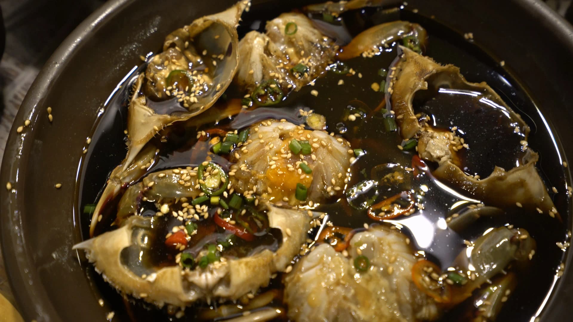 Ganjang gejang served in a stone pot with glossy soy sauce marinade topped with sesame seeds and spring onions