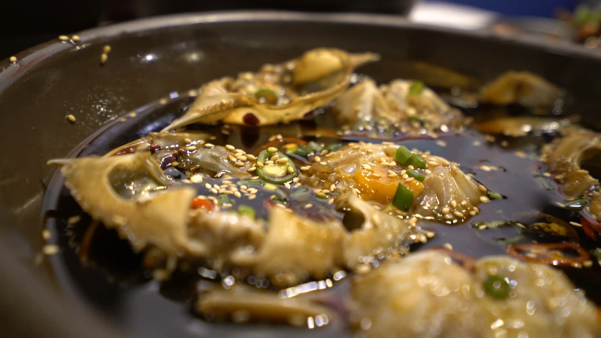 Side view of soy marinated crab showing soy sauce soaked up to the shell edges with translucent cured crab meat visible