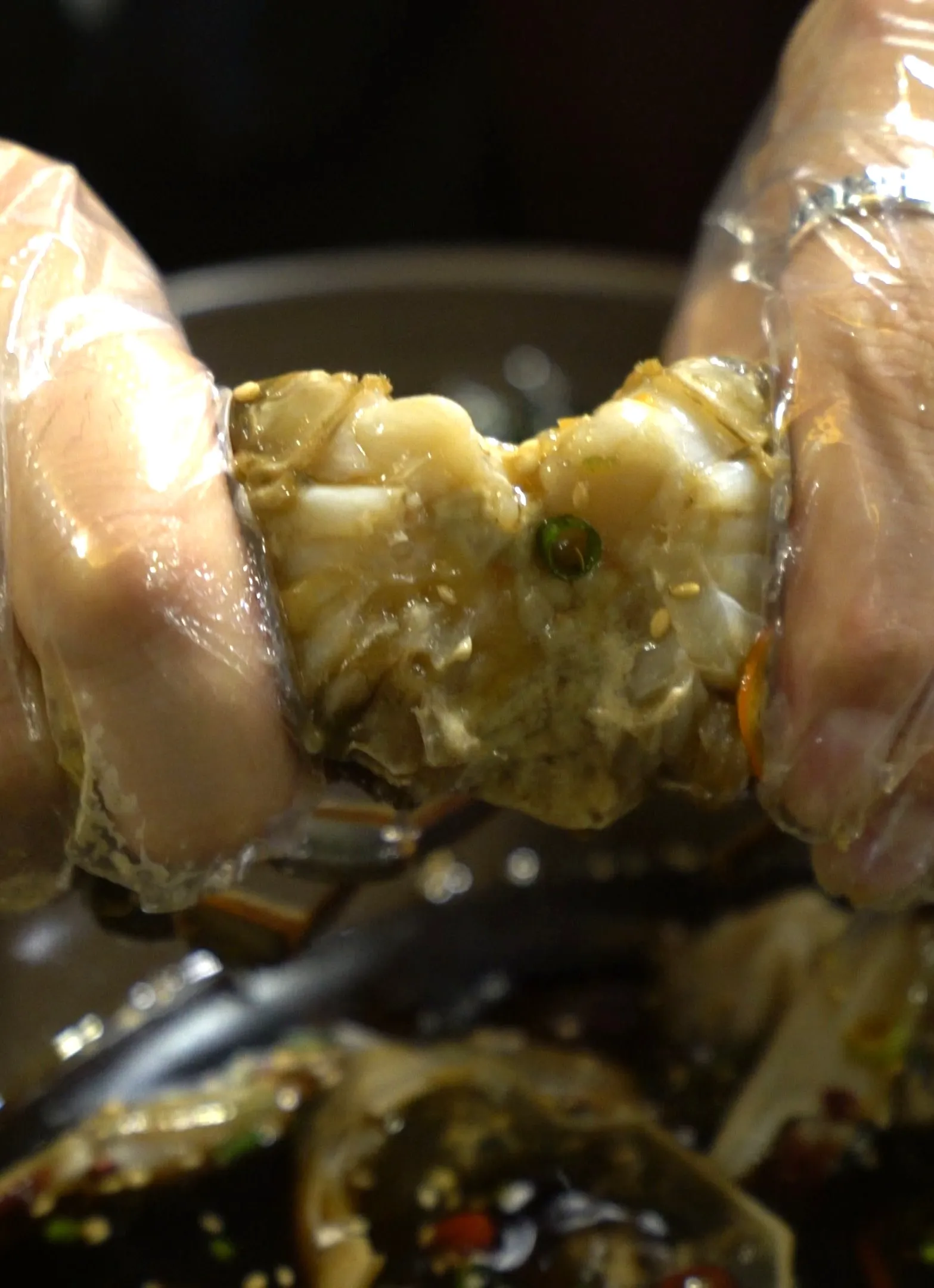 Hands wearing plastic gloves snapping a crab leg in half revealing soy-marinated crab meat inside
