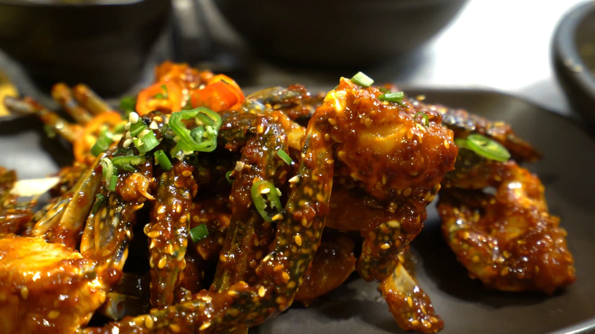 Gloved hands cracking open a spicy yangnyeom gejang crab leg with red chilli sauce coating the meat