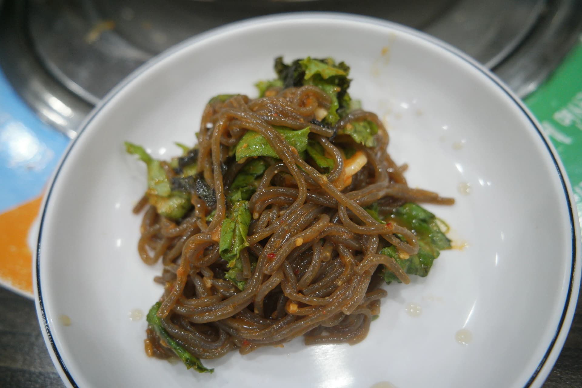 Nærbillede af makguksu — syrlige boghvedenudler løftet op med spisepinde | 하이제이에스비