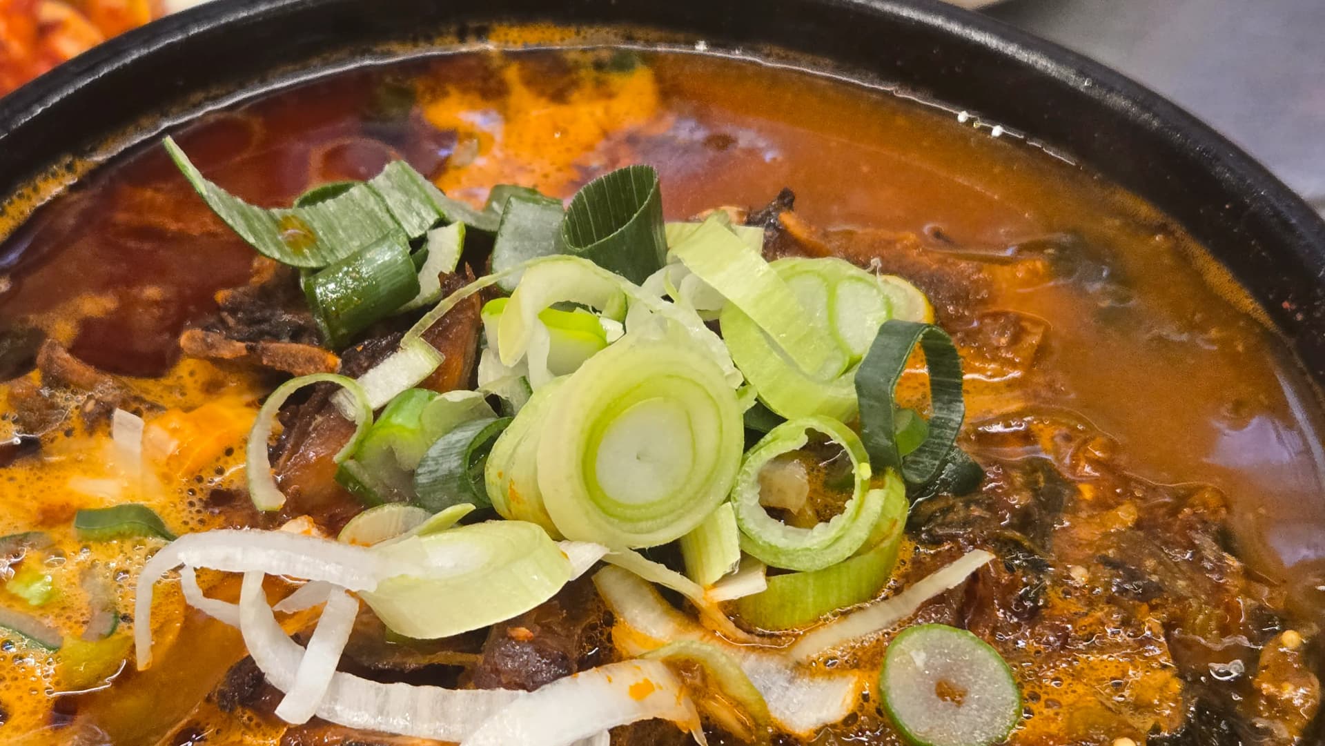 ພາບໃກ້ໆຂອງຊຸບກະດູກໝູທີ່ກຳລັງເດືອດ ມີຕົ້ນຫອມສົດຫັ່ນໂຮຍໄວ້ຂ້າງເທິງ | 하이제이에스비