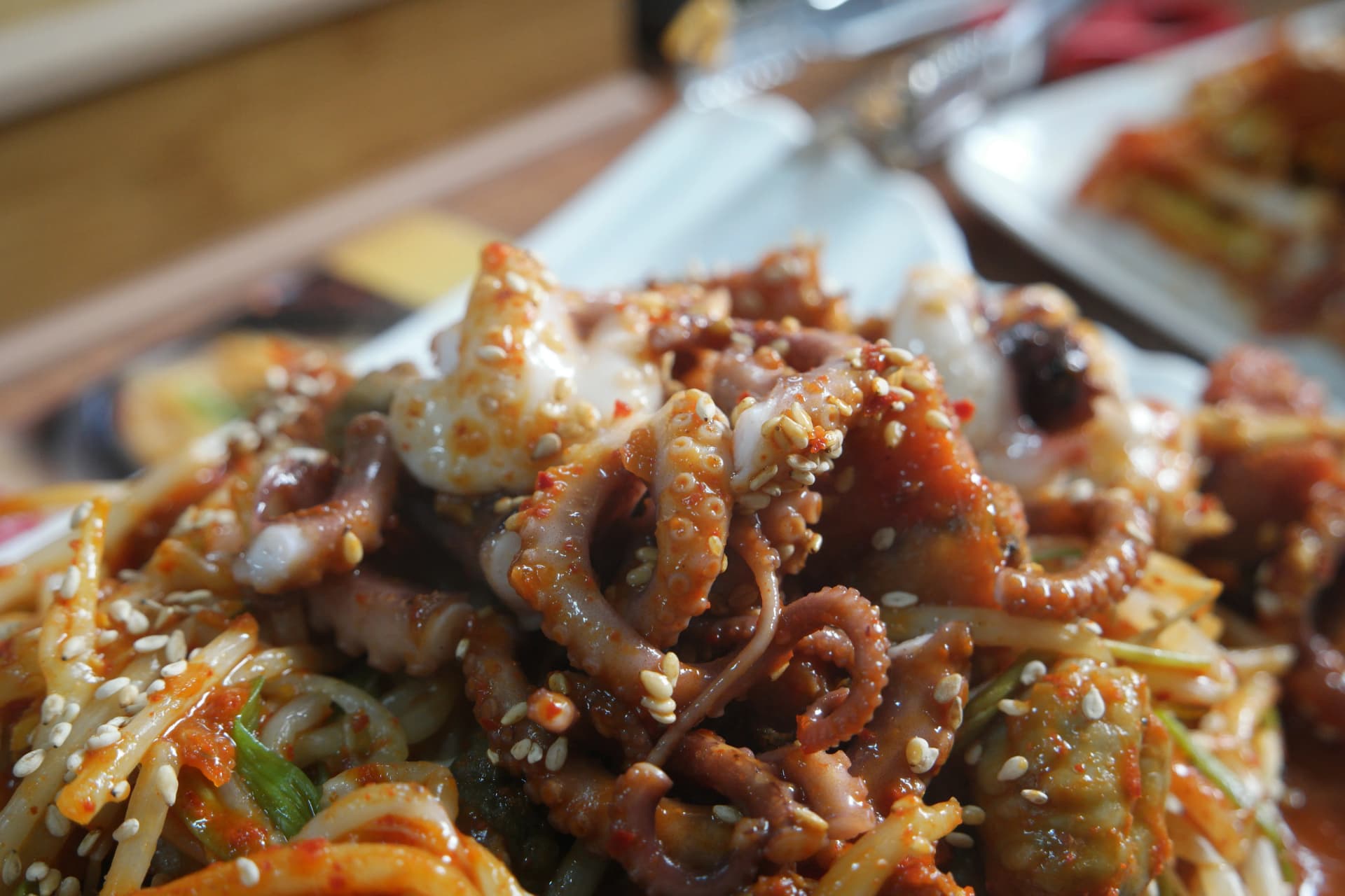 لقطة قريبة لأذرع الأخطبوط بالصلصة الحمراء مع حبات السمسم في الطبق الحار