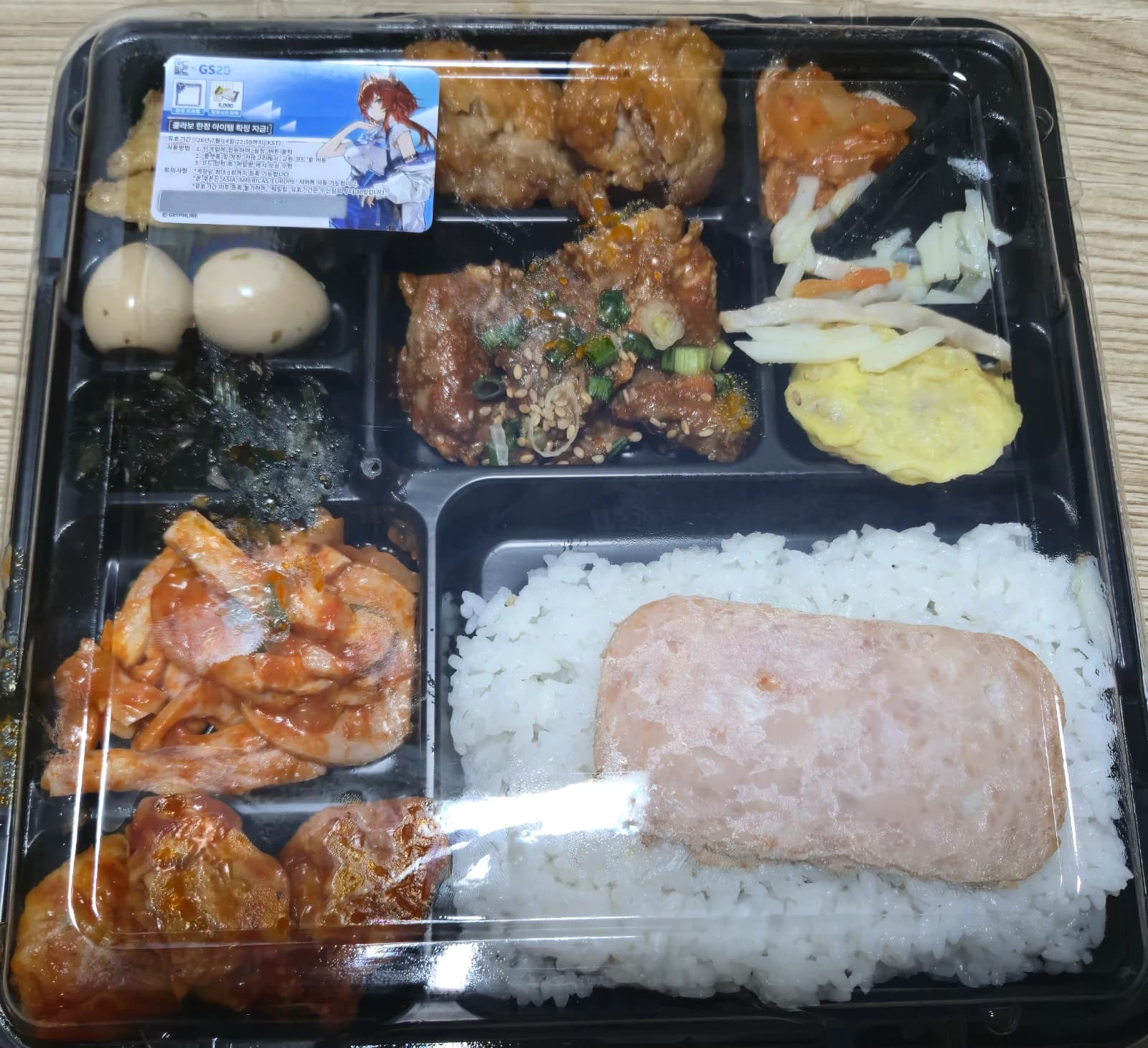 ヘジャロウン弁当2のフタを開けた状態 スパム 赤い味付け肉 うずら卵 のり佃煮 卵焼きなどおかずがぎっしり