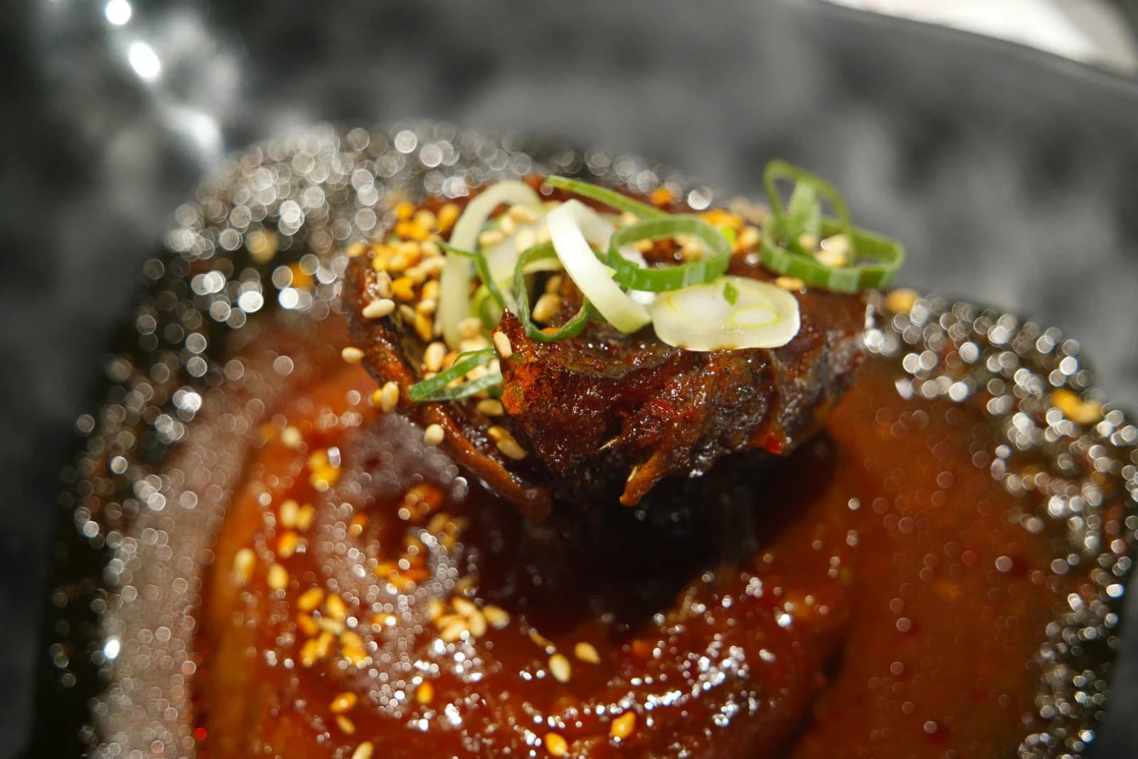 Braised mackerel appetizer in a small dish with soy glaze, sesame seeds, and chopped scallions on top