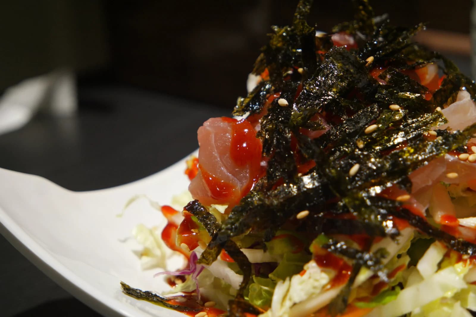 Close-up of spicy raw fish salad with chojang sauce dripping over sashimi slices and sesame seeds peeking through seaweed