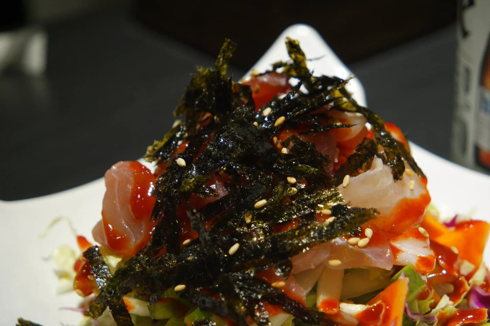 Overhead view of raw fish salad showing translucent sashimi tinted pink from chojang sauce beneath shredded seaweed