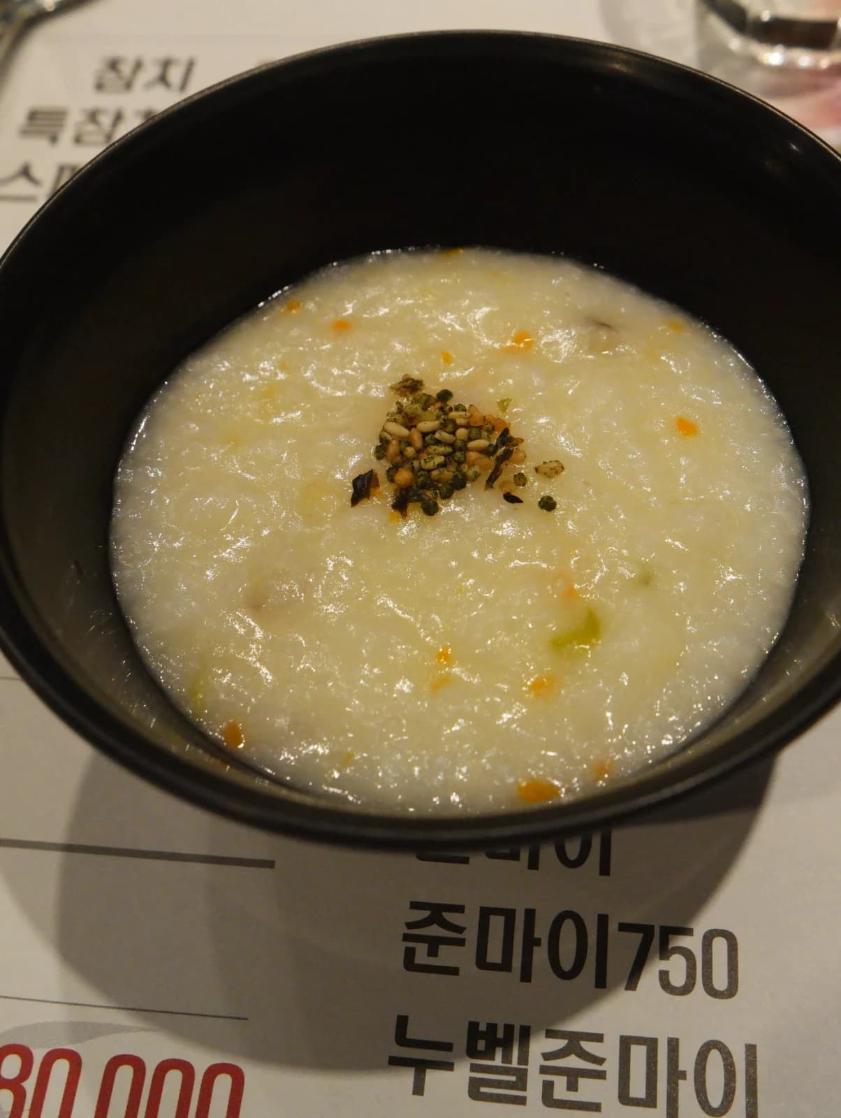 Full bowl of Korean abalone porridge, creamy white rice porridge topped with pine nuts and sesame seeds