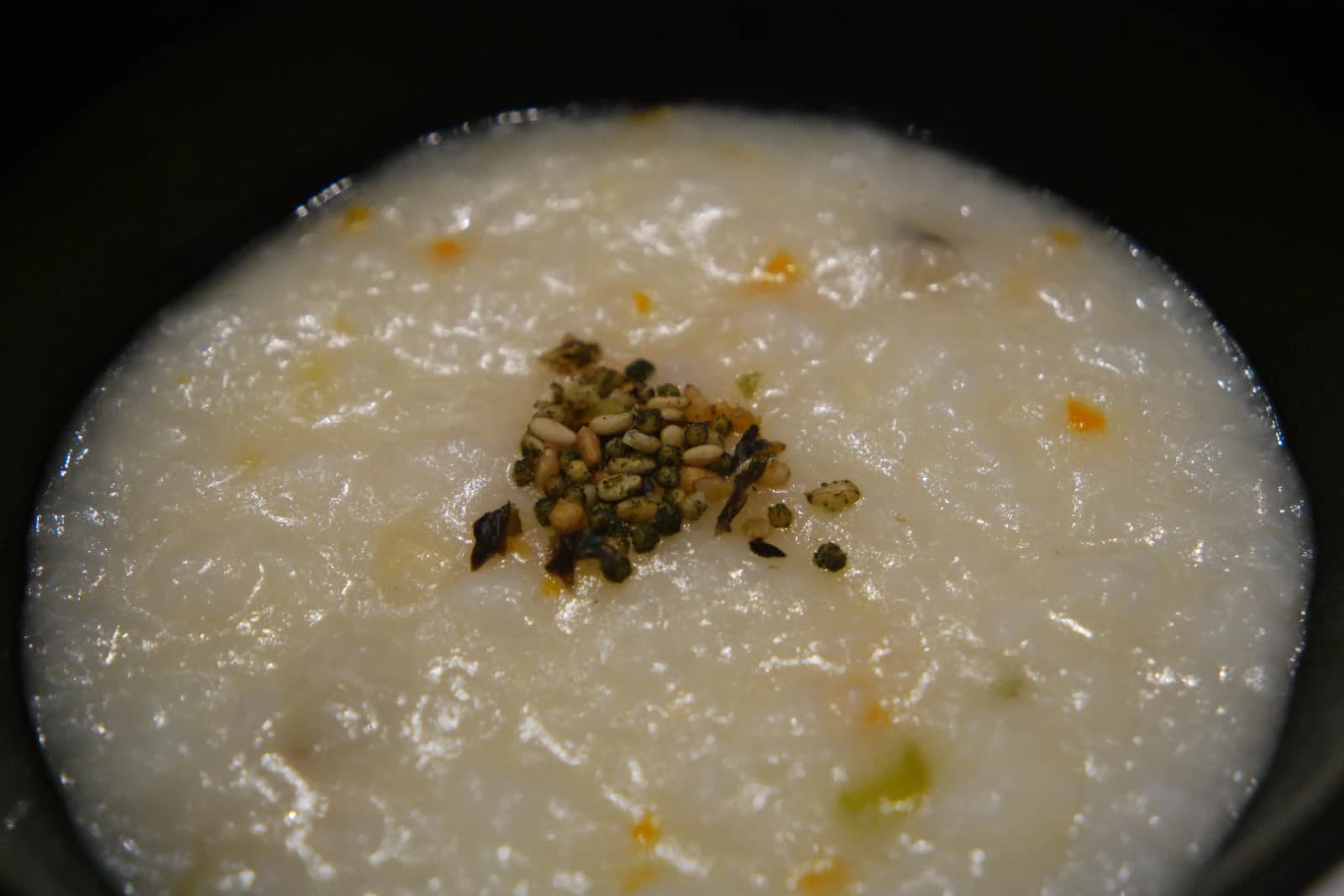 Spoonful of abalone porridge lifted from the bowl, showing its thick creamy texture