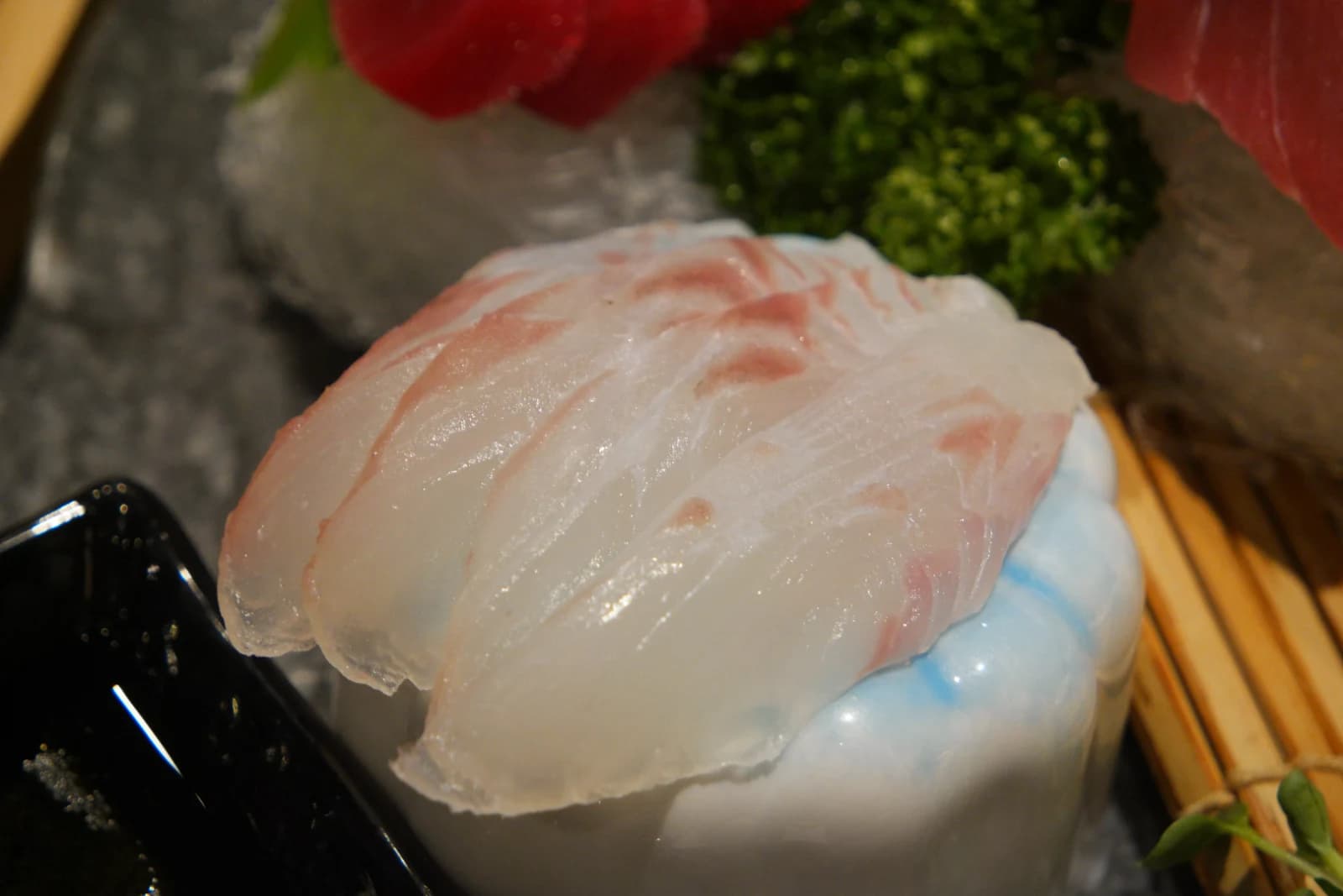 Flounder sashimi on a bamboo mat, translucent white flesh glistening in the light