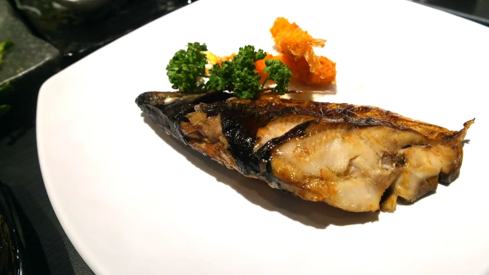 Grilled mackerel served mid-course with golden crispy skin and white flaky flesh visible underneath