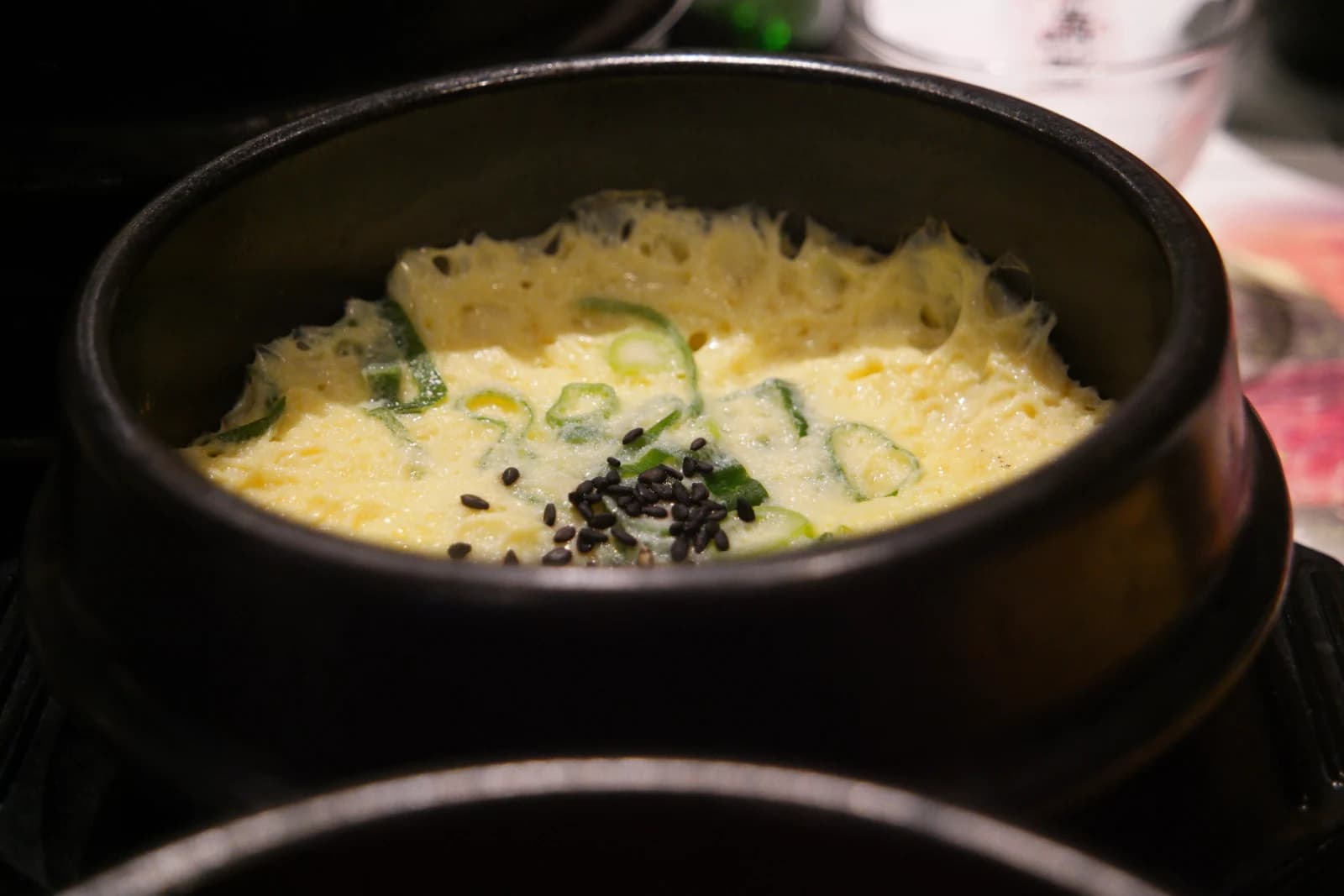 Korean steamed egg custard in a hot stone pot, fluffy and bubbly with black sesame and scallions on top
