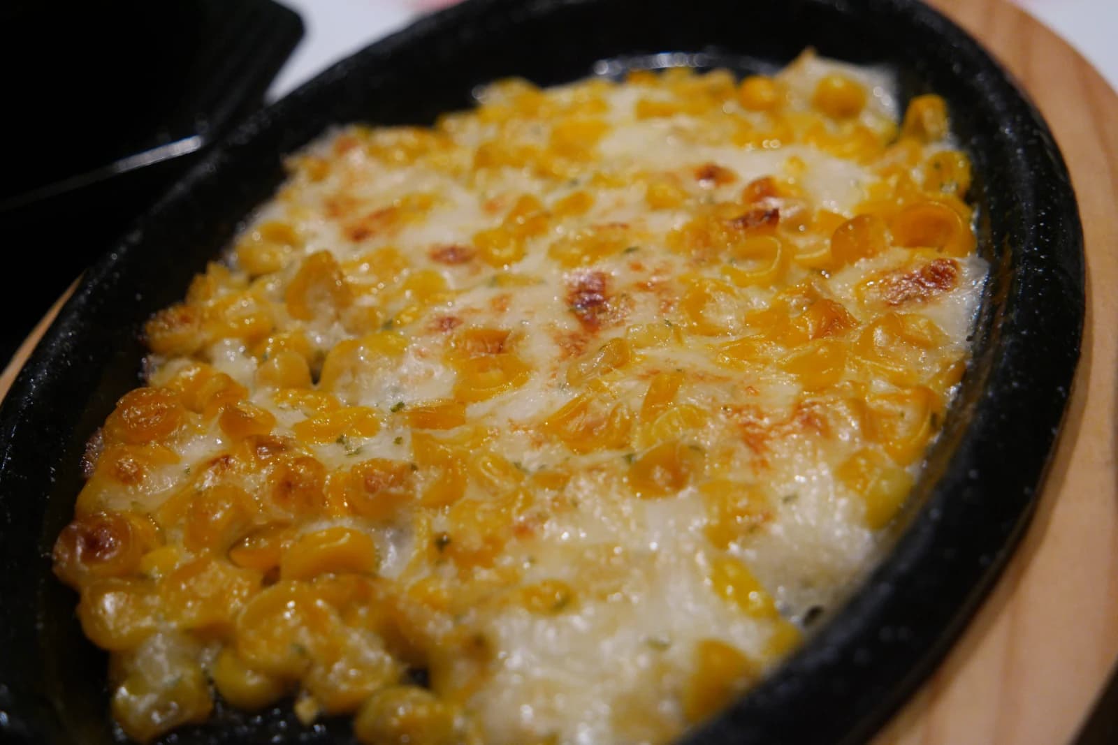 Corn cheese bubbling on a hot iron plate with melted cheese over sweet corn kernels