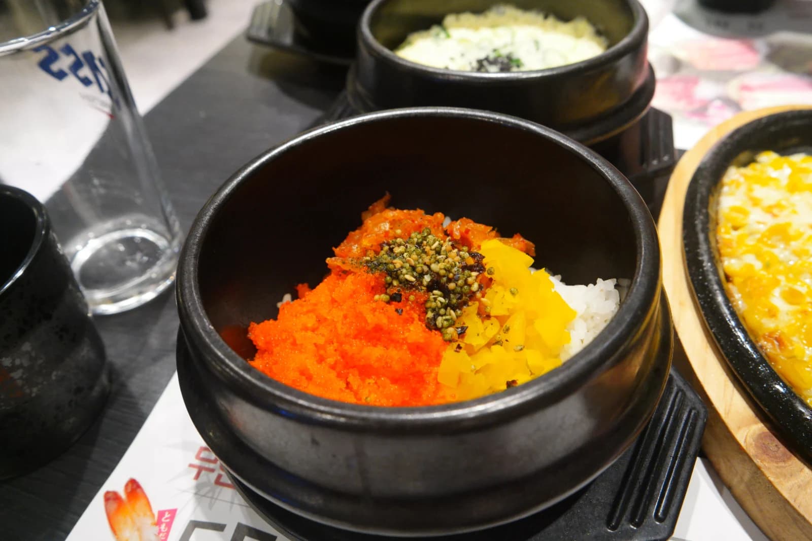 Korean roe rice in a stone pot with bright orange flying fish roe heaped on white rice, yellow pickled radish and sesame on the side