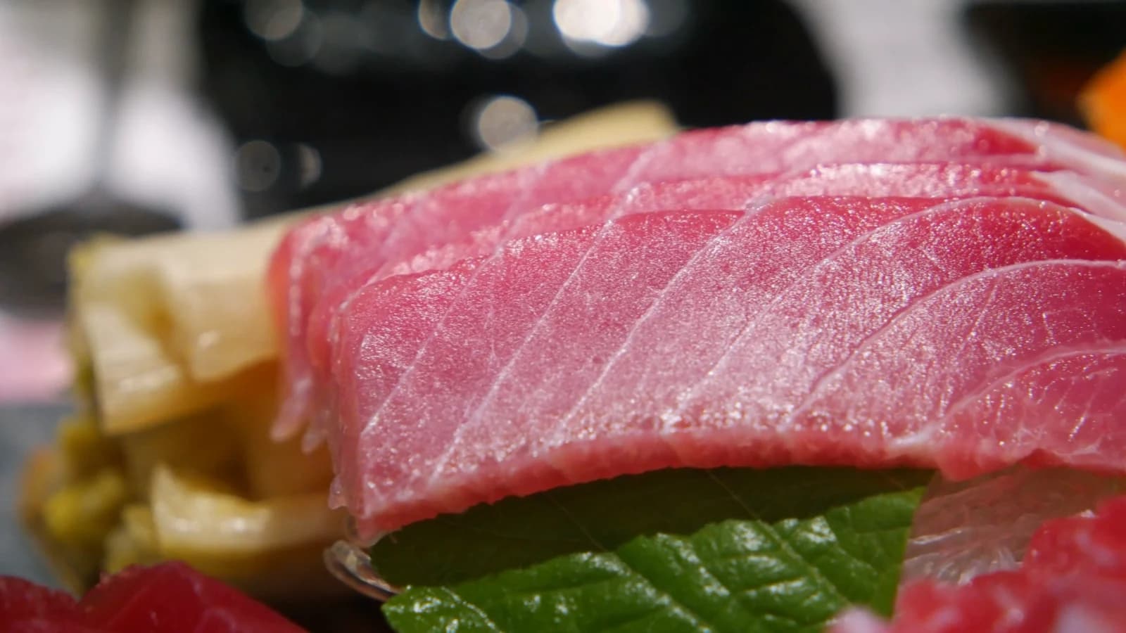 Medium-fatty tuna belly from another angle showing pink-toned marbling along the grain with pickled ginger on the side