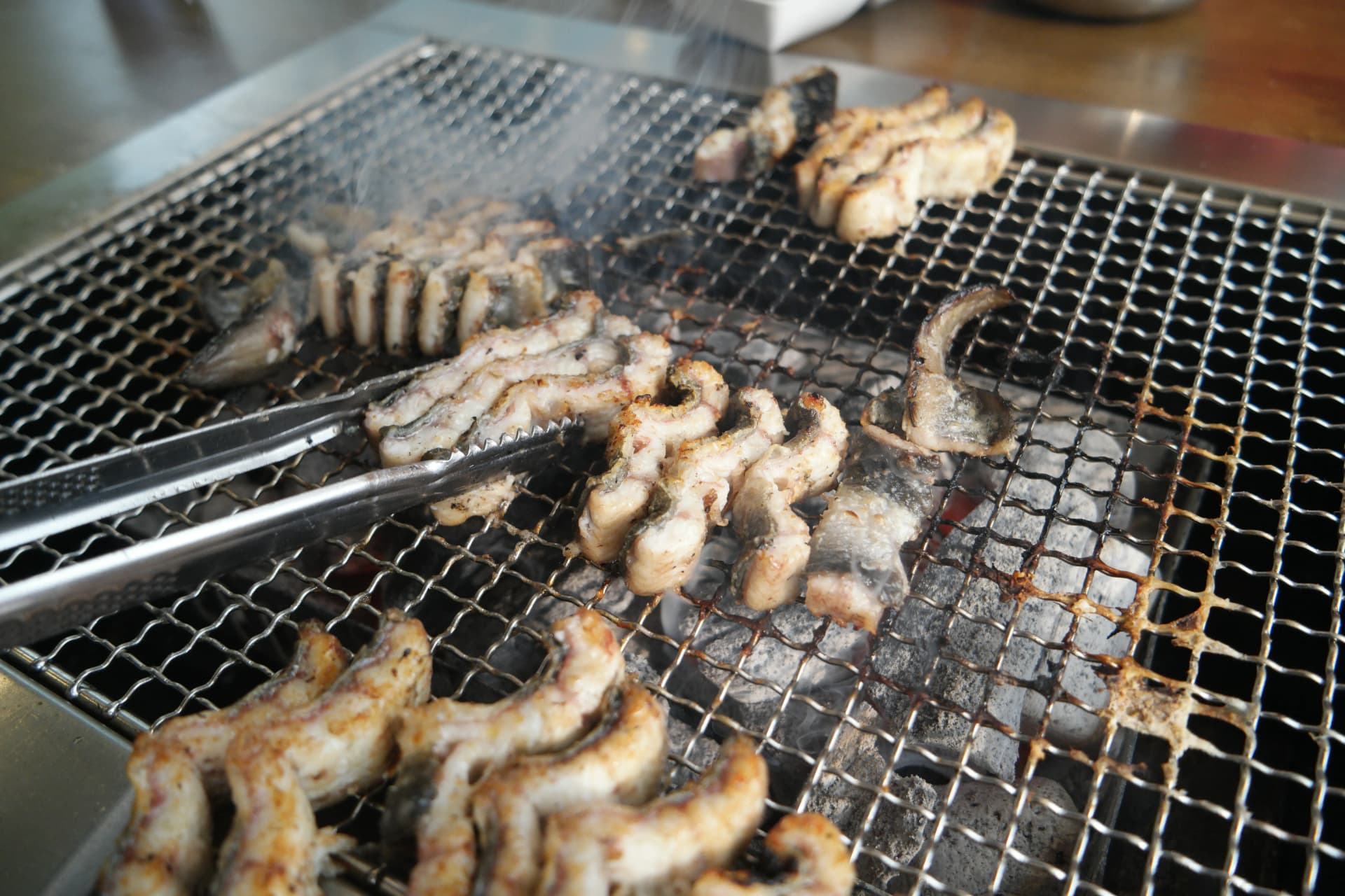 직원이 집게로 민물장어를 하나하나 뒤집으며 골고루 익히는 모습 | 하이제이에스비