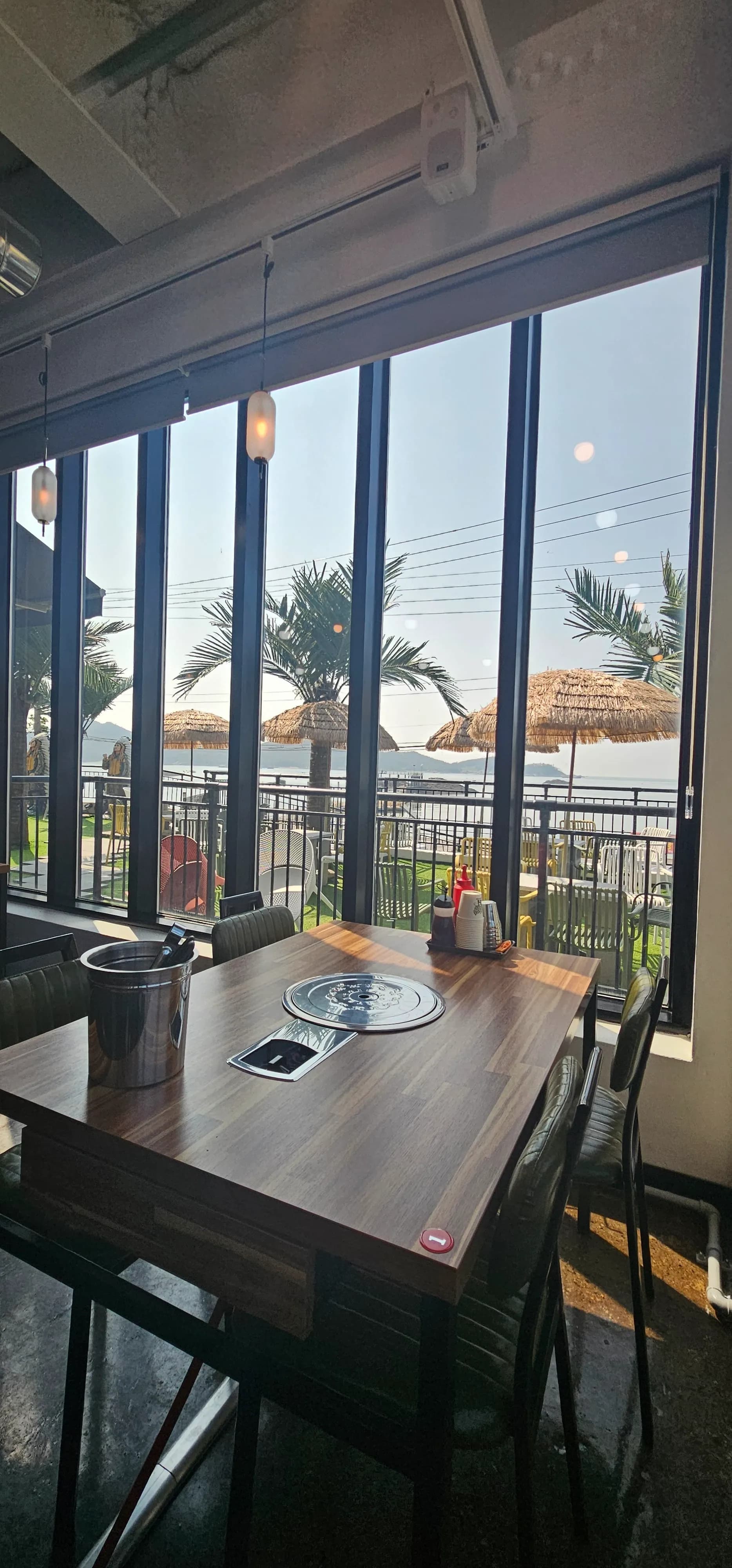 통유리 창가 너머로 바다와 야자수 테라스가 보이는 해산물 식당 내부 | 하이제이에스비