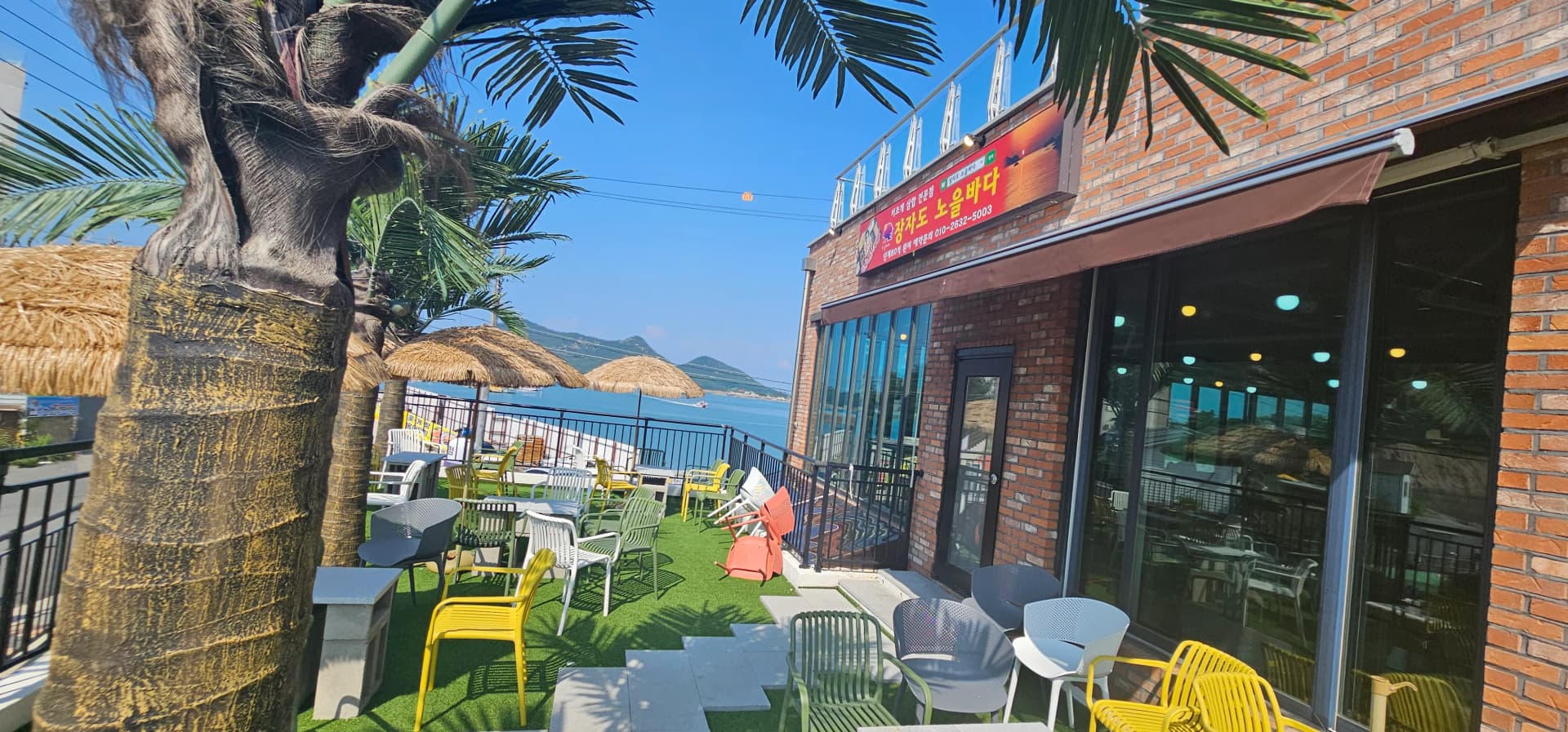 붉은 벽돌 건물 외관과 알록달록한 의자가 놓인 바다 앞 테라스 | 하이제이에스비