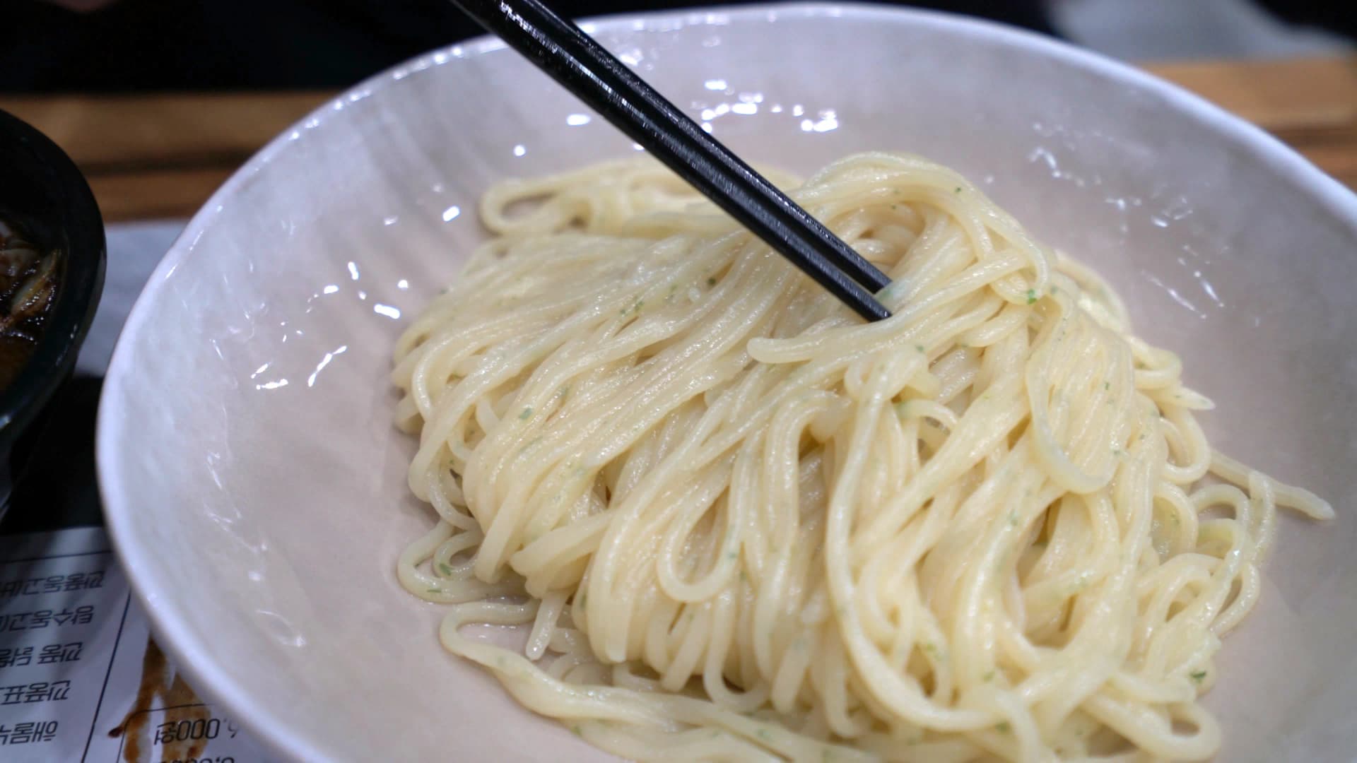 وعاء نودلز بيضاء بجانب وعاء صوص كانجاجانغ أسود، النودلز لوحدها في وعاء والصوص في وعاء ثاني منفصل