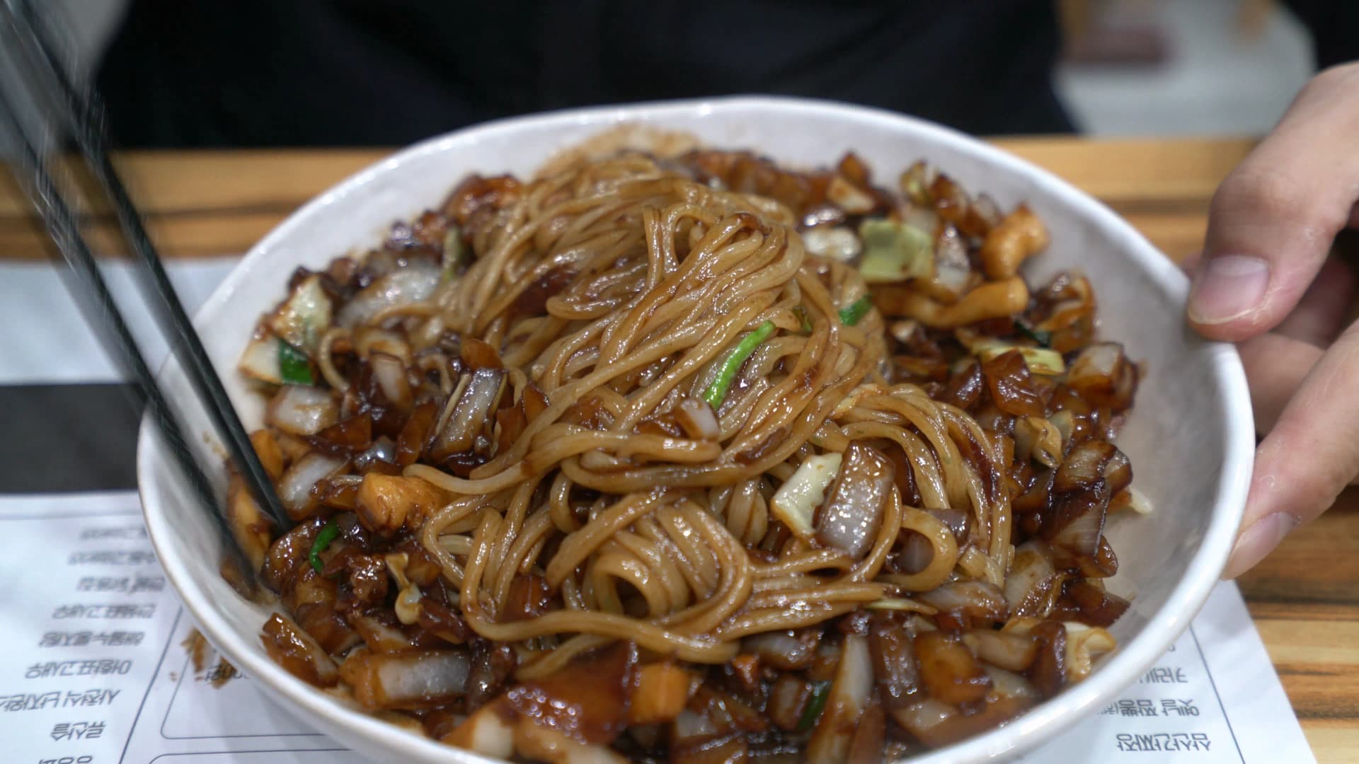 بداية خلط الكانجاجانغ بالعيدان، النودلز البيضاء بدأت تتلوّن بالصوص الأسود أثناء رفعها وتقليبها