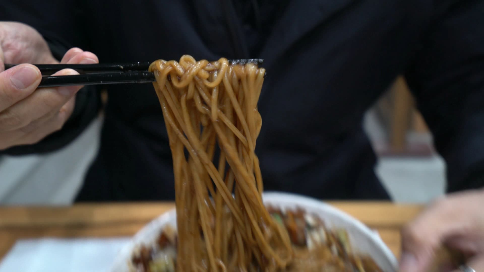كانجاجانغ جاهز، عيدان ترفع النودلز عالياً وكل شعيرة مغلّفة بصوص التشونجانغ الأسود اللامع بشكل متساوي