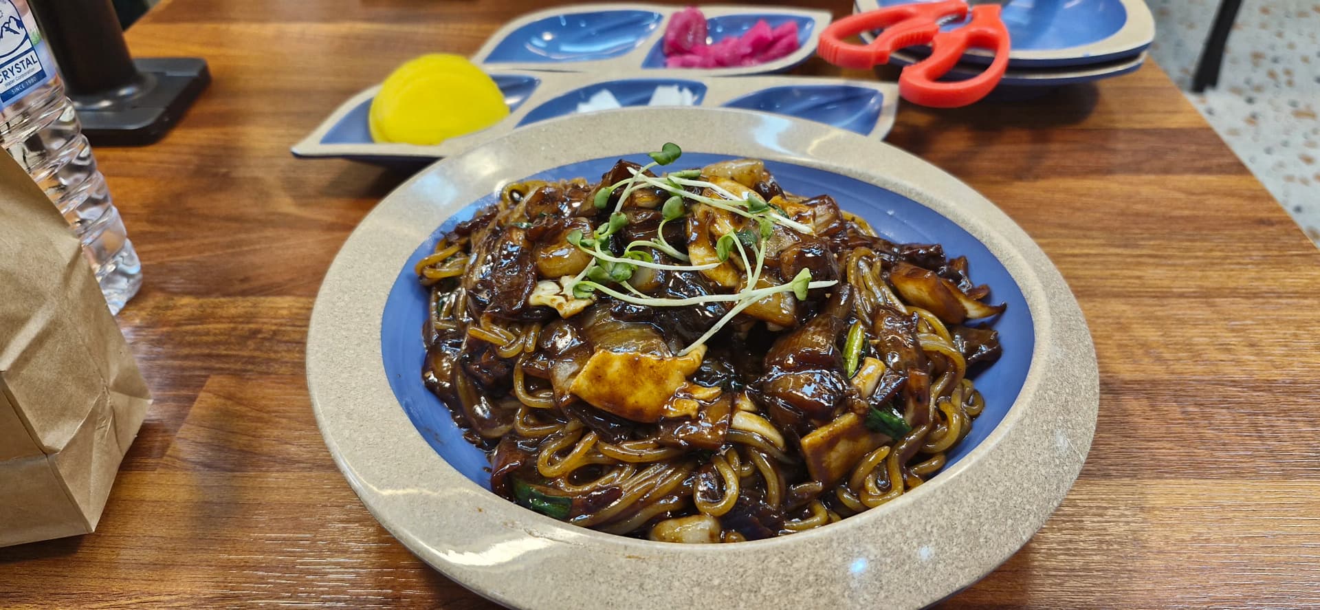 لقطة قريبة لسامسون جاجانغ تبيّن النودلز المخلوطة مع الصوص وبراعم خضراء وقطع مأكولات بحرية بين الشعيرات