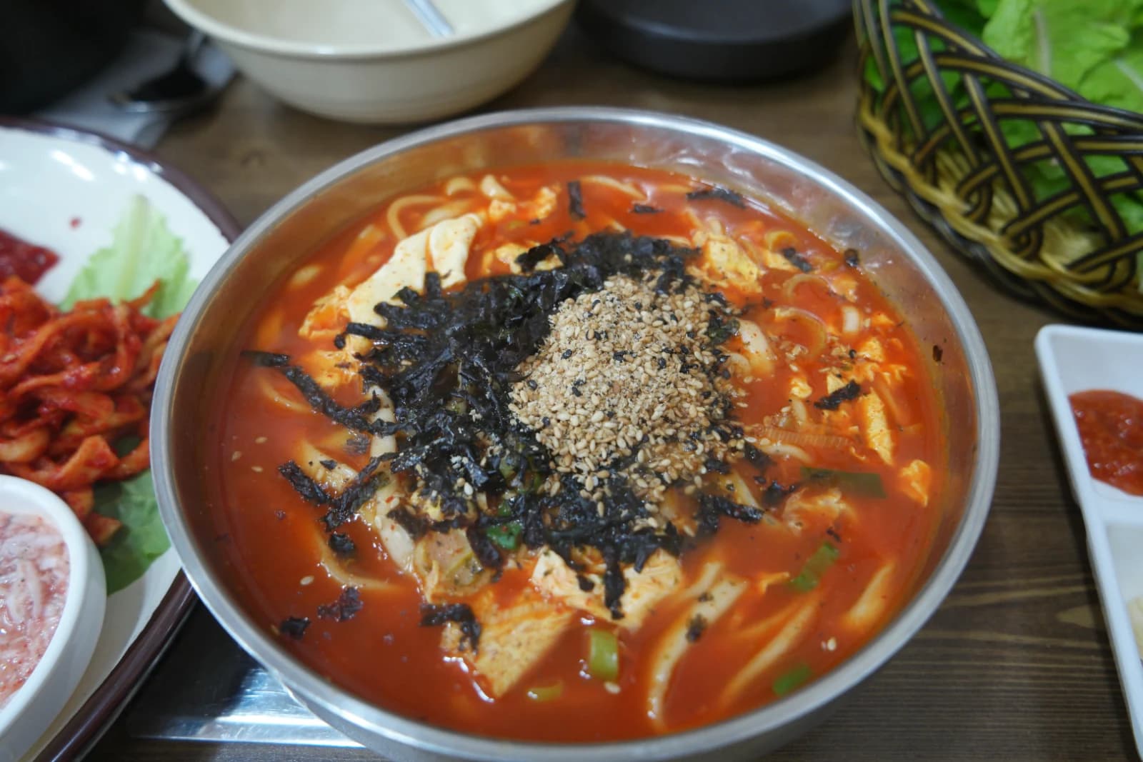 Bowl of spicy kalguksu with red broth topped with seaweed flakes and sesame seeds
