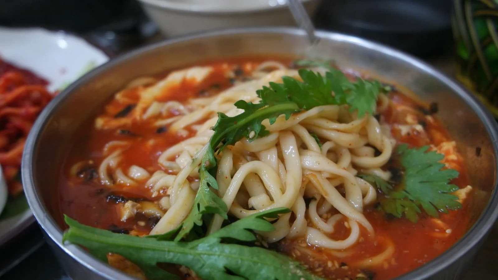 Spicy kalguksu with crown daisy mixed into the noodles and broth looking deeper in color