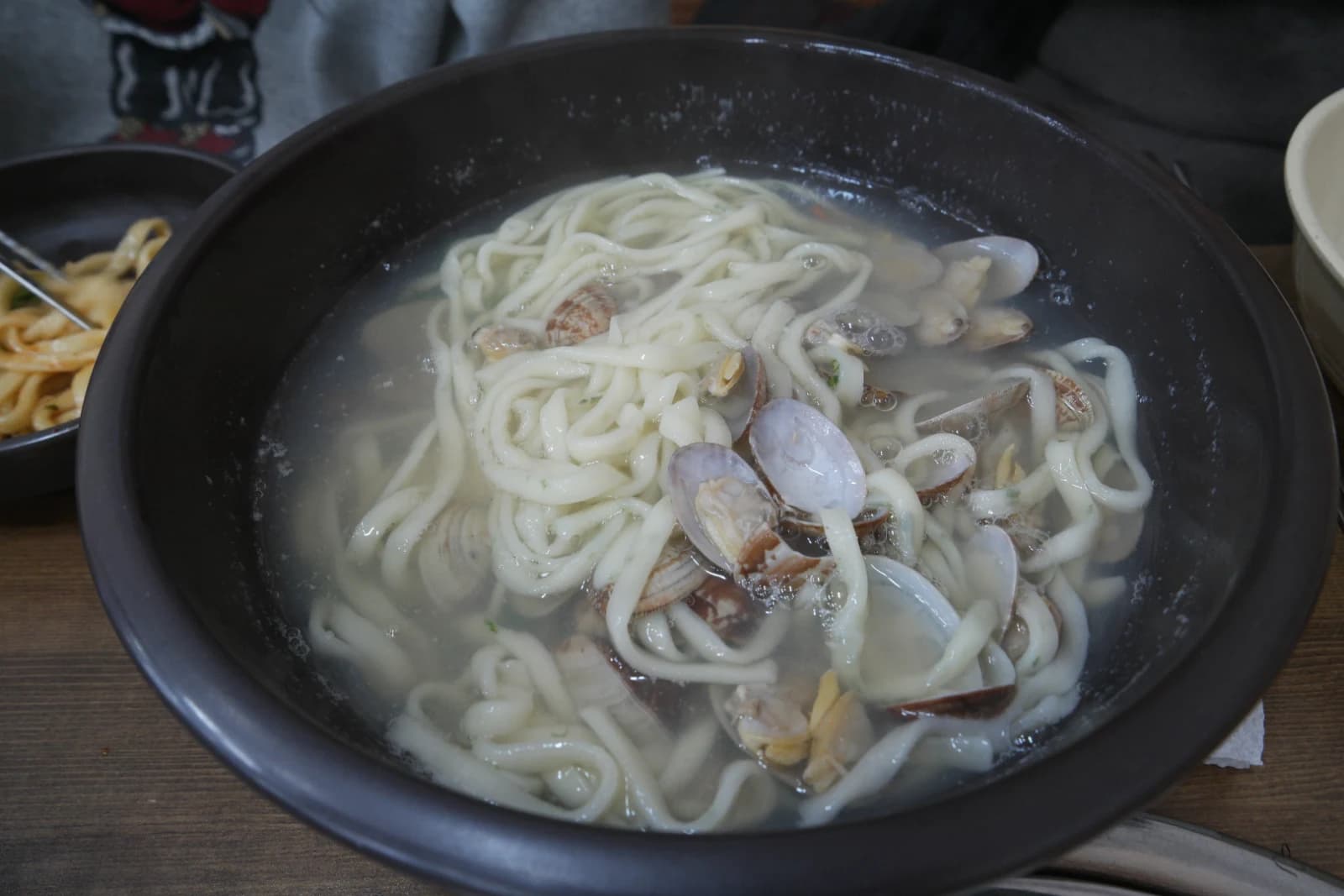 Bowl of clam kalguksu with clear broth and clam shells scattered among the noodles