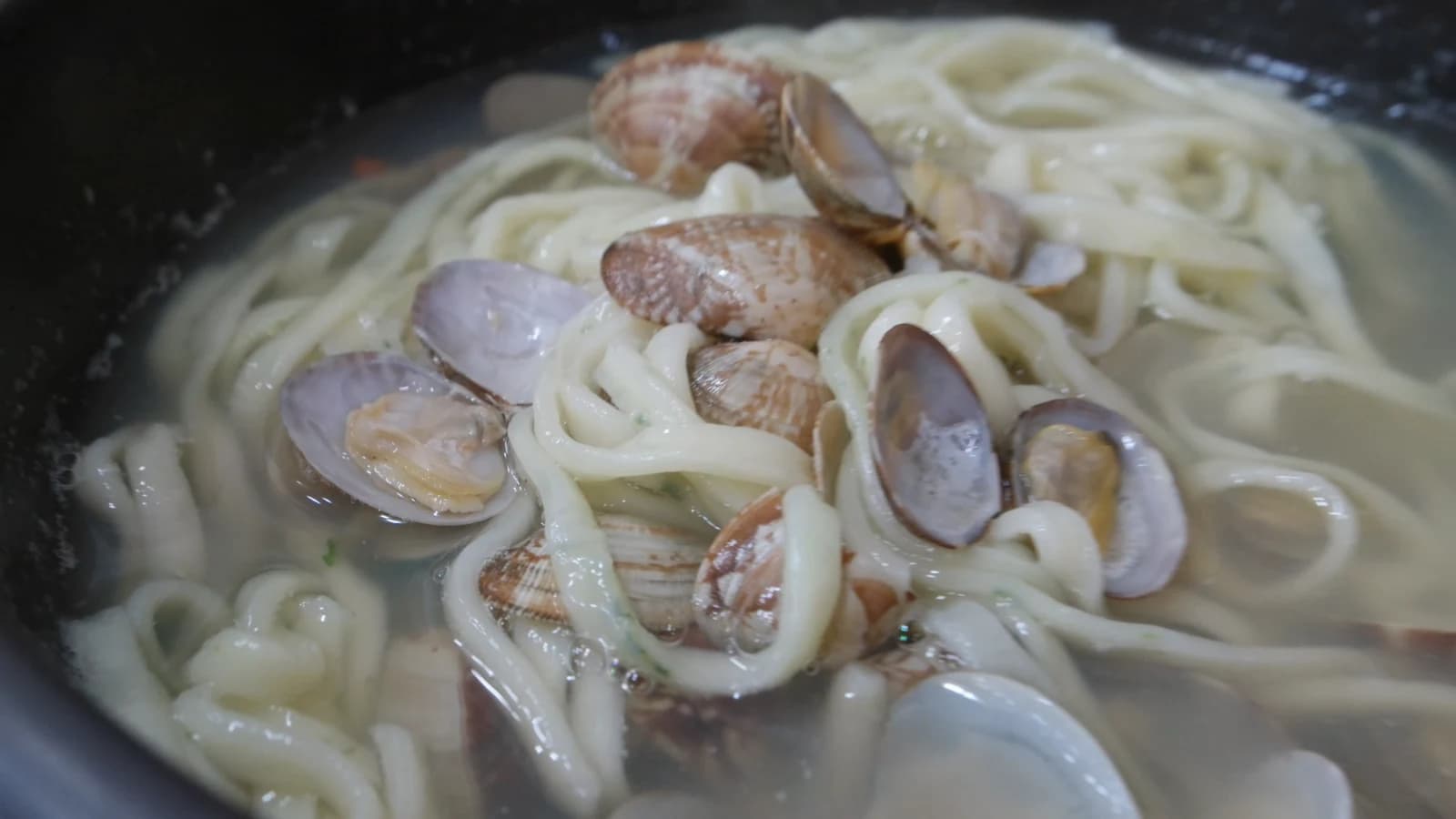 Close-up of an open clam in the kalguksu bowl showing the meat inside the shell