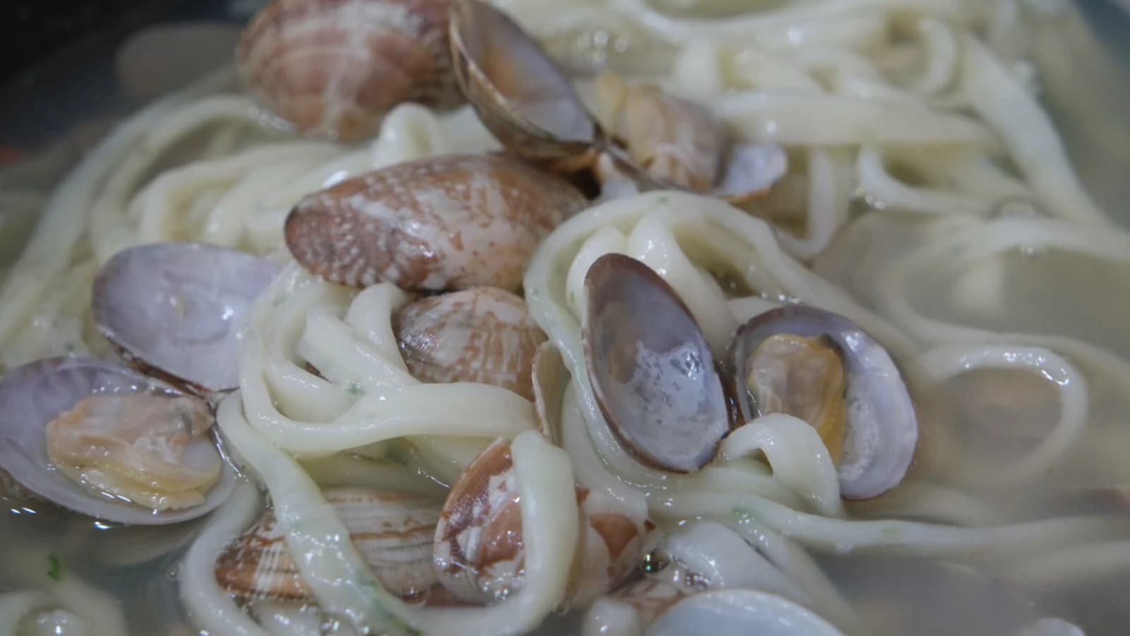 Open clam shell in kalguksu broth with plump clam meat nestled inside