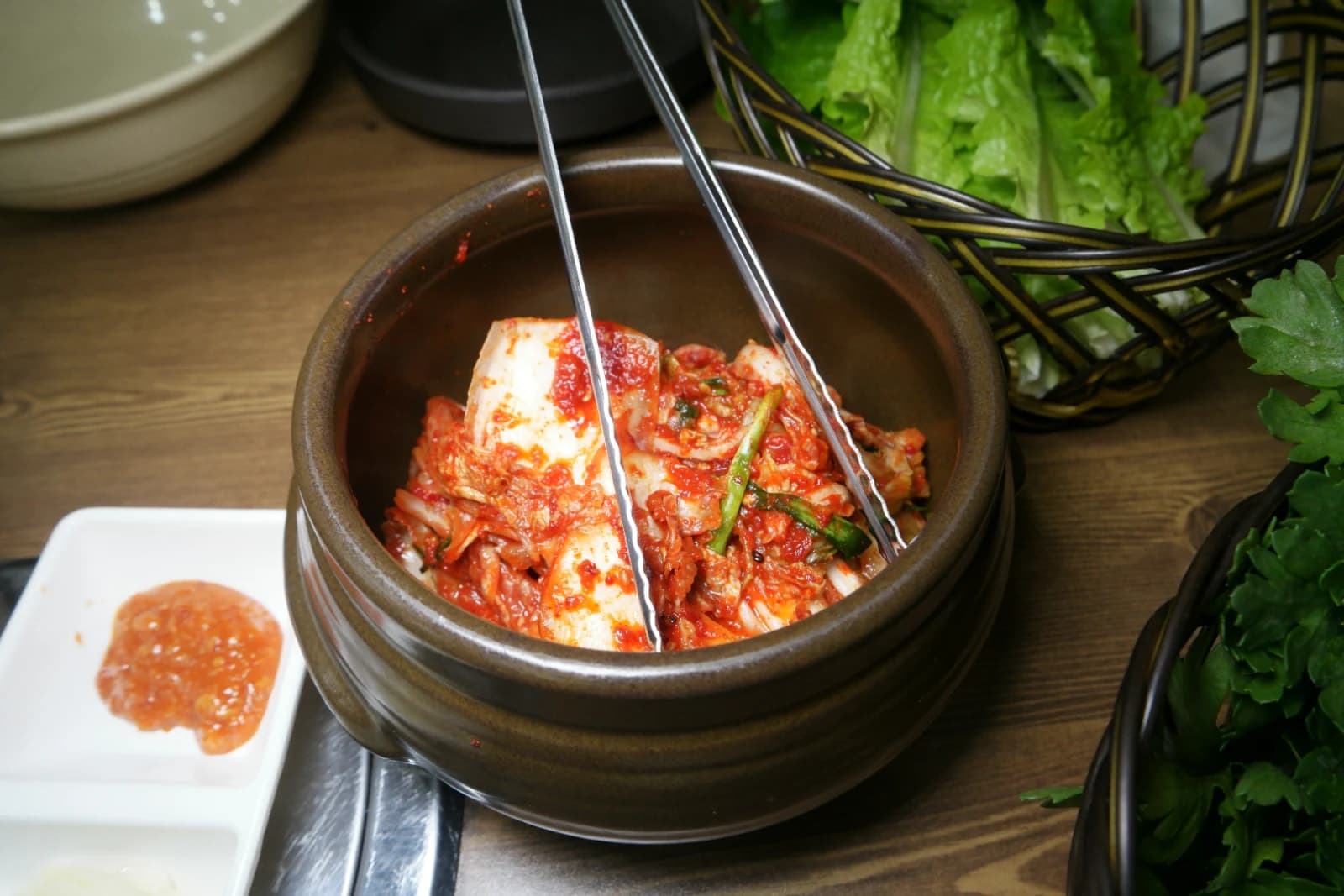 Chopsticks pulling bossam kimchi from a jar showing napa cabbage coated in bright red chili seasoning