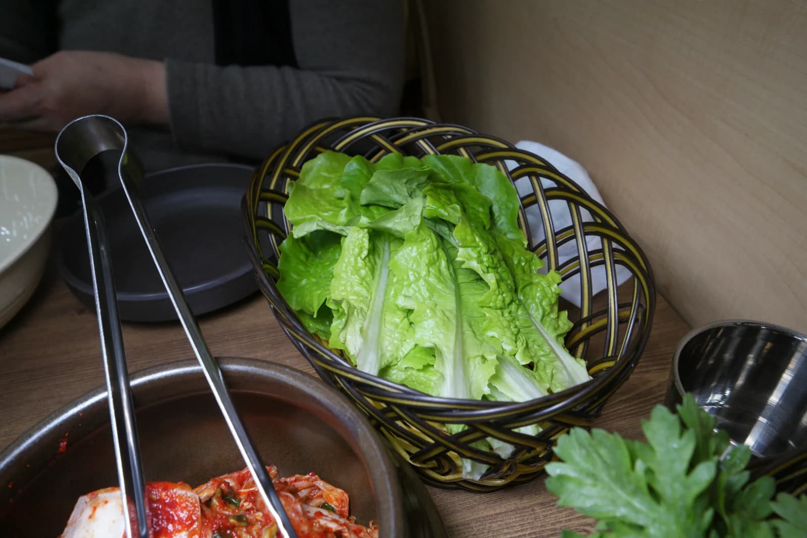 Basket overflowing with fresh green lettuce leaves next to a kimchi jar and crown daisy basket