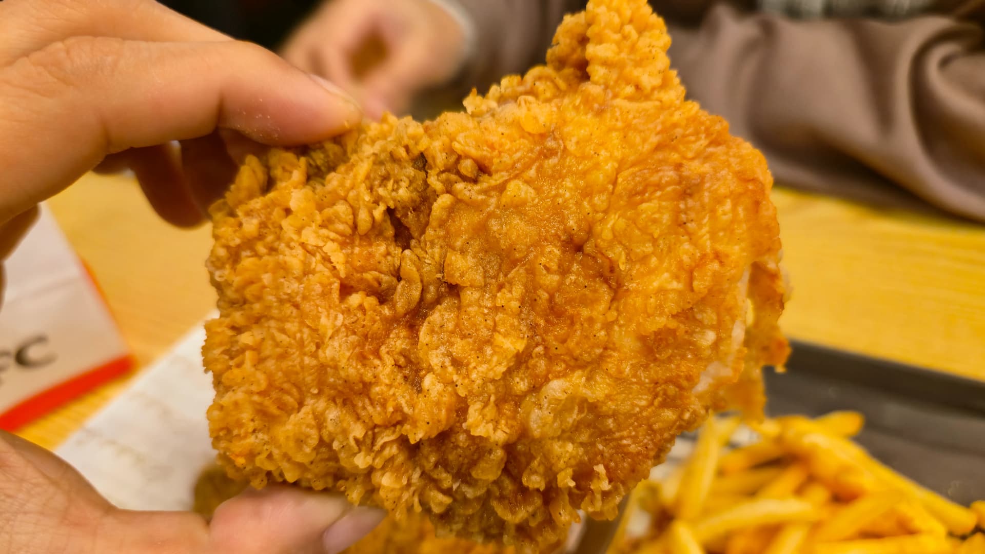한국 KFC 가슴살 치킨 한 조각을 손으로 들고 있는 모습 손바닥보다 큰 크기