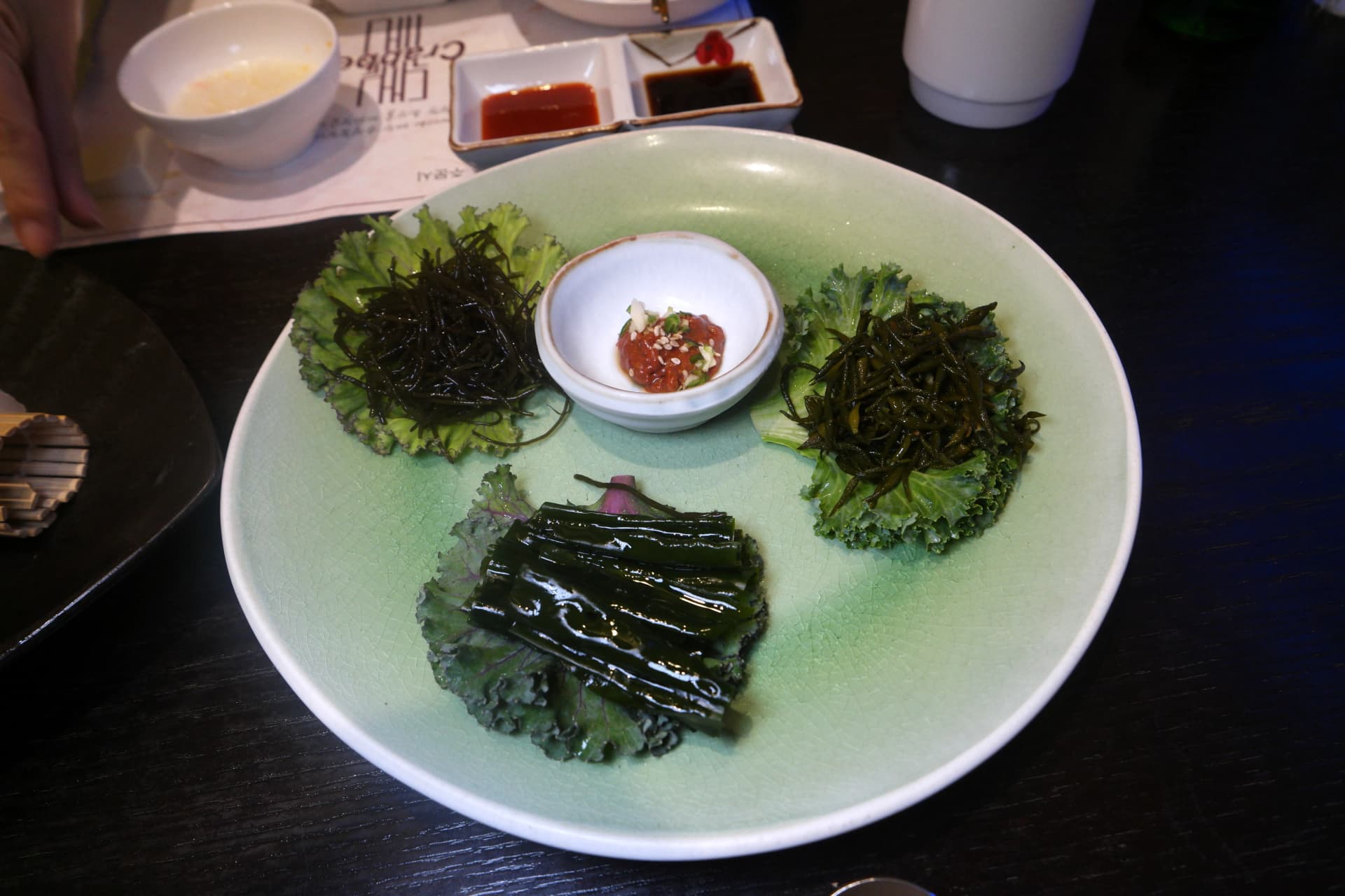 Plato con tres variedades de algas coreanas sobre col rizada y salsa de vinagre picante en el centro | 하이제이에스비