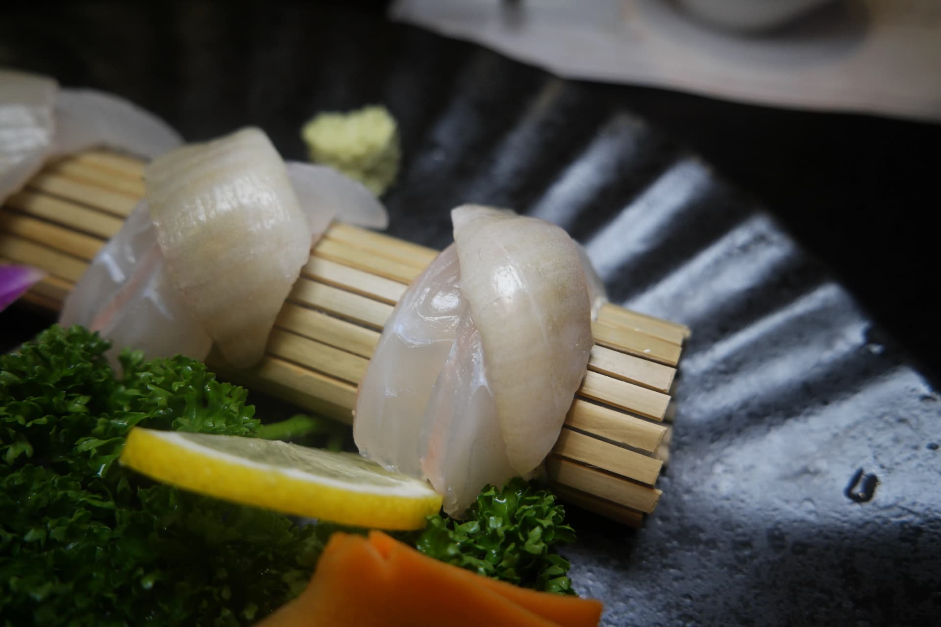 Sashimi de lenguado visto desde el lado de la guarnición de limón y zanahoria, destacando el grosor generoso de los cortes | 하이제이에스비