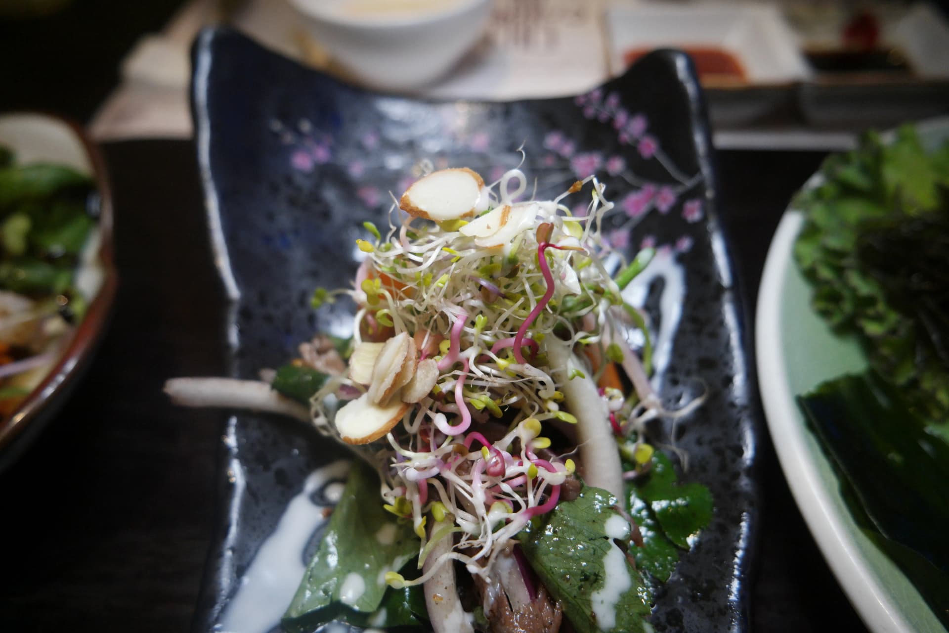 Vista general de la mesa con ensalada de brotes, algas y otros acompañamientos dispuestos juntos | 하이제이에스비