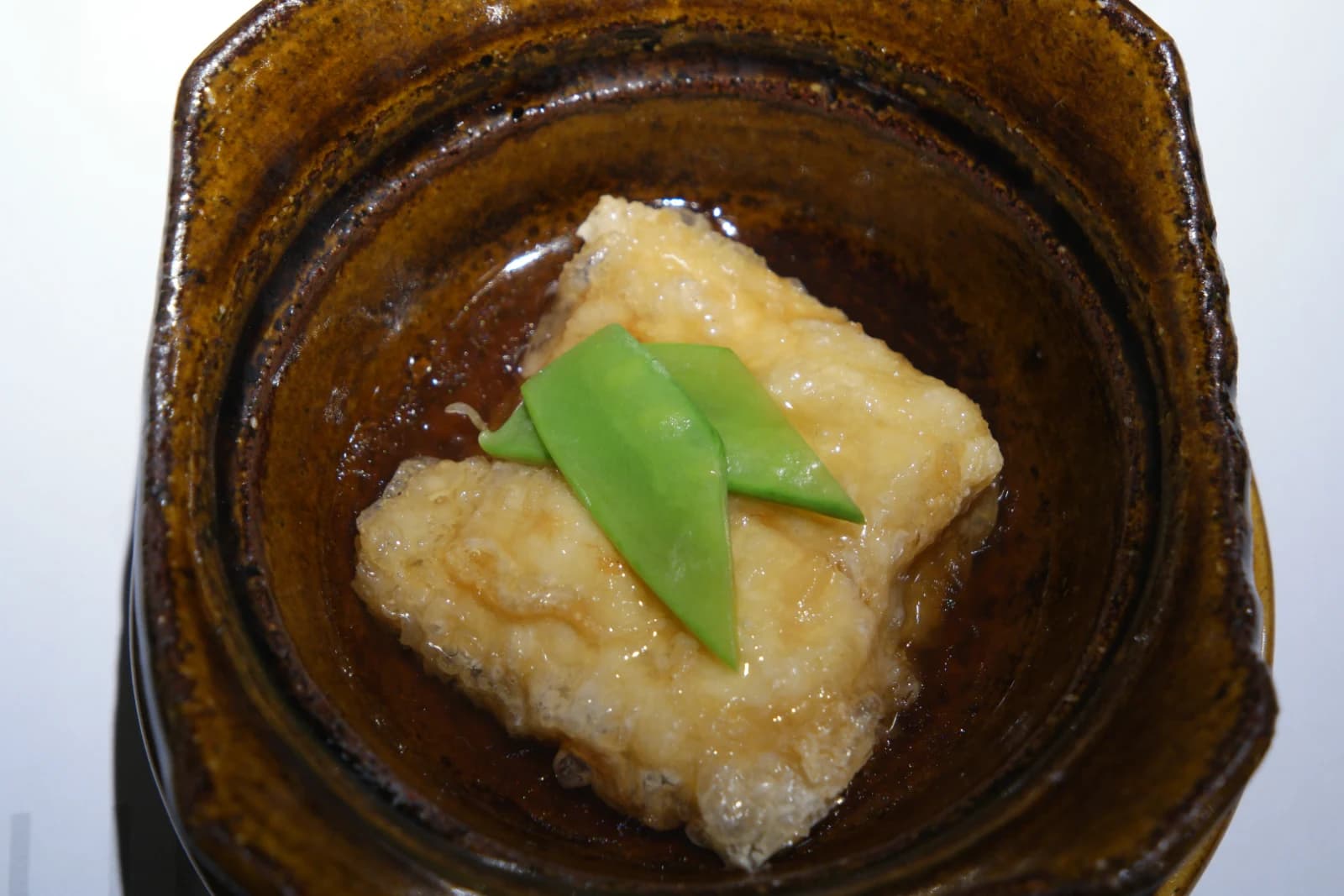 Tofu agedashi soulevé aux baguettes révélant l'intérieur fondant et crémeux