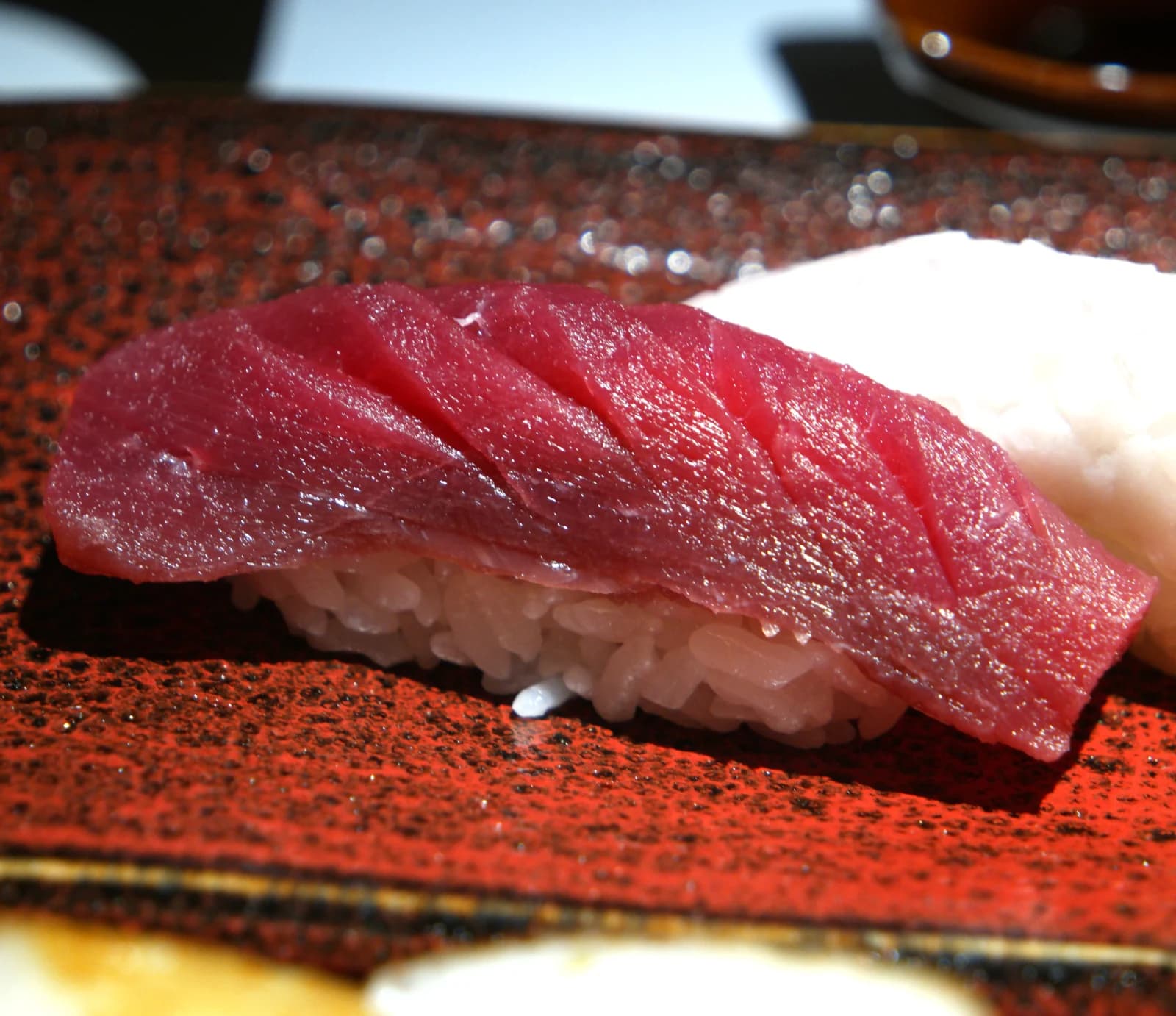 Sushi de thon levé aux baguettes, chair rouge rubis brillante posée sur le riz